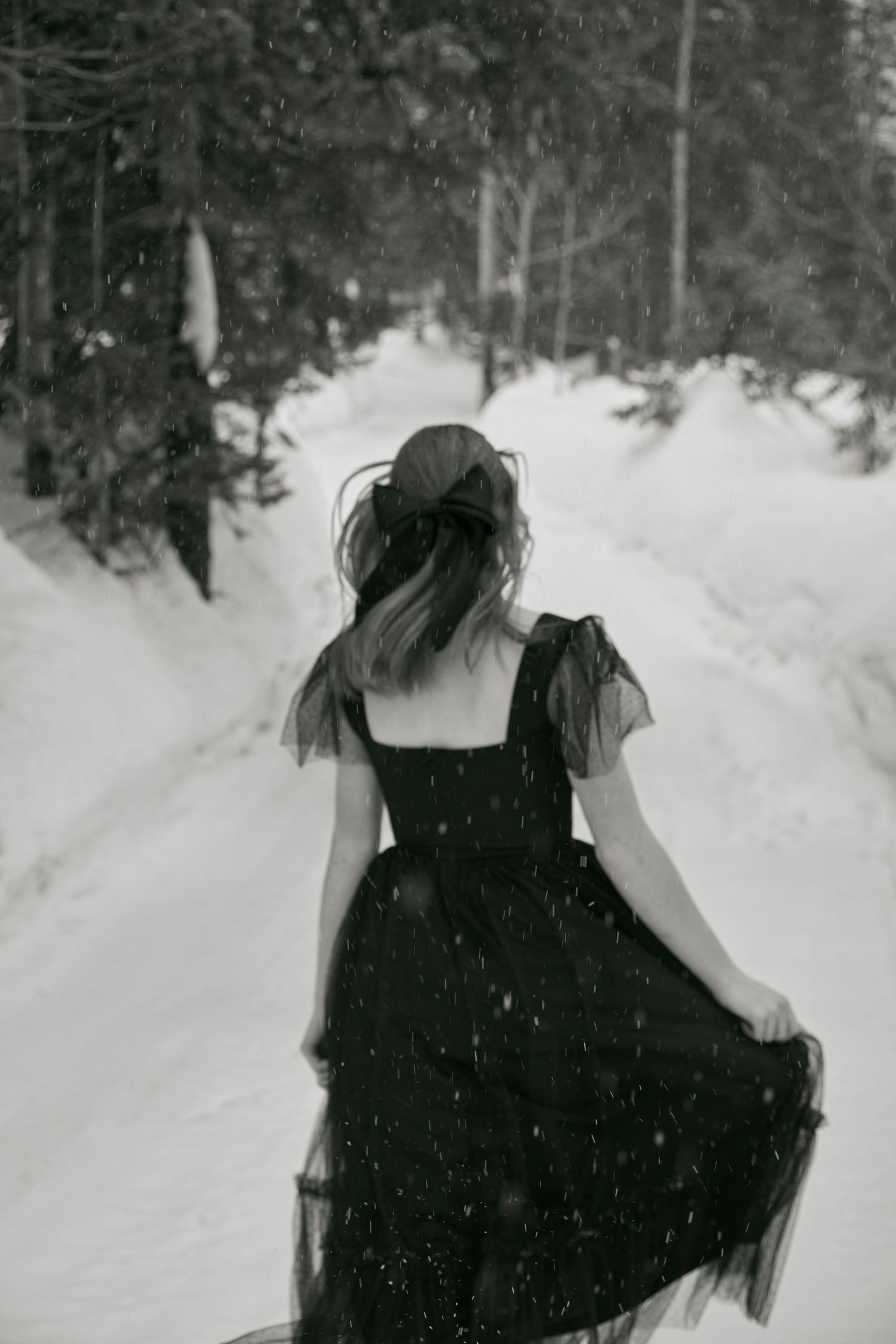 A black dress twirls against a snowy forest path in a dreamy winter scene.