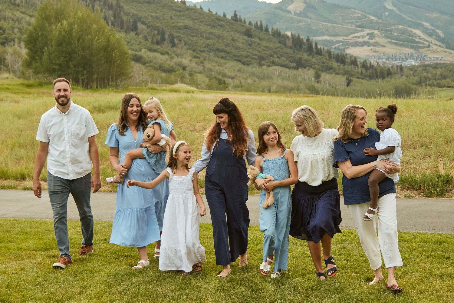 A large family group poses together on a grassy hillside in coordinated blue and white outfits.
