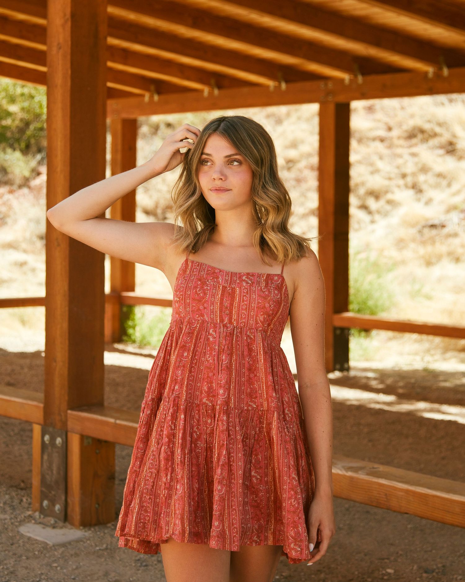 Summer portrait under wooden pergola wearing coral sundress in desert setting.