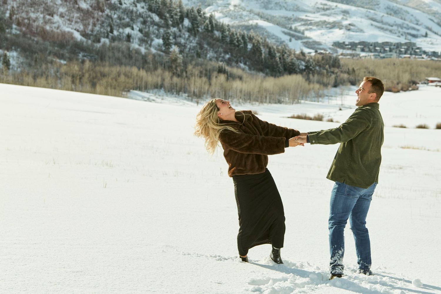 Couple dancing and spinning in snow with mountains in background.