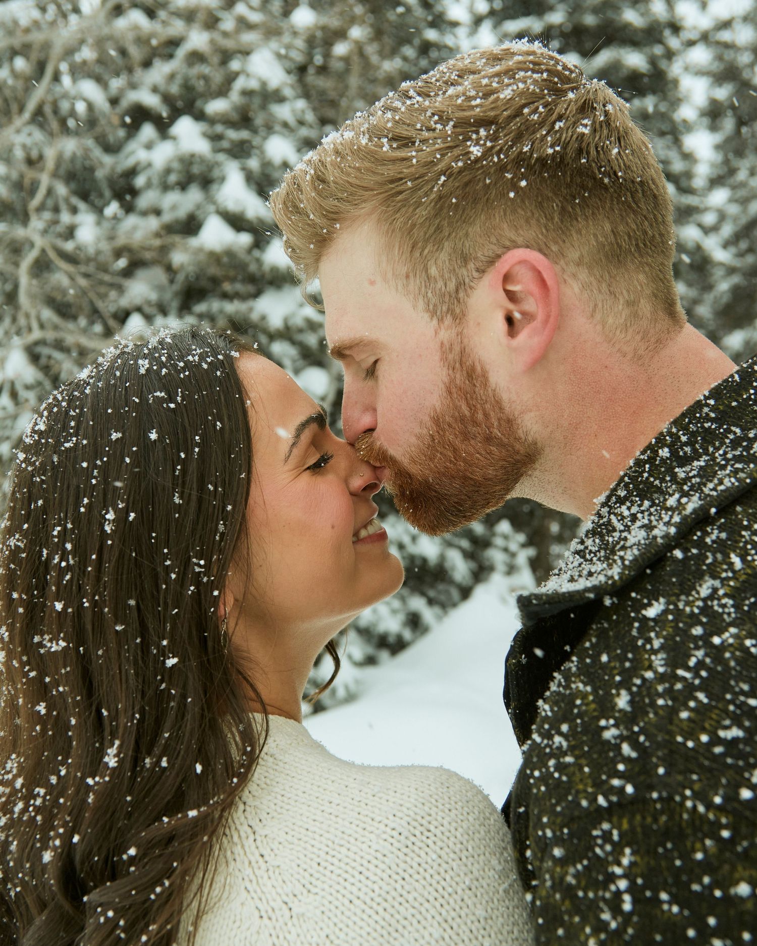 Intimate winter portrait with snowflakes falling around couple in cozy sweaters.