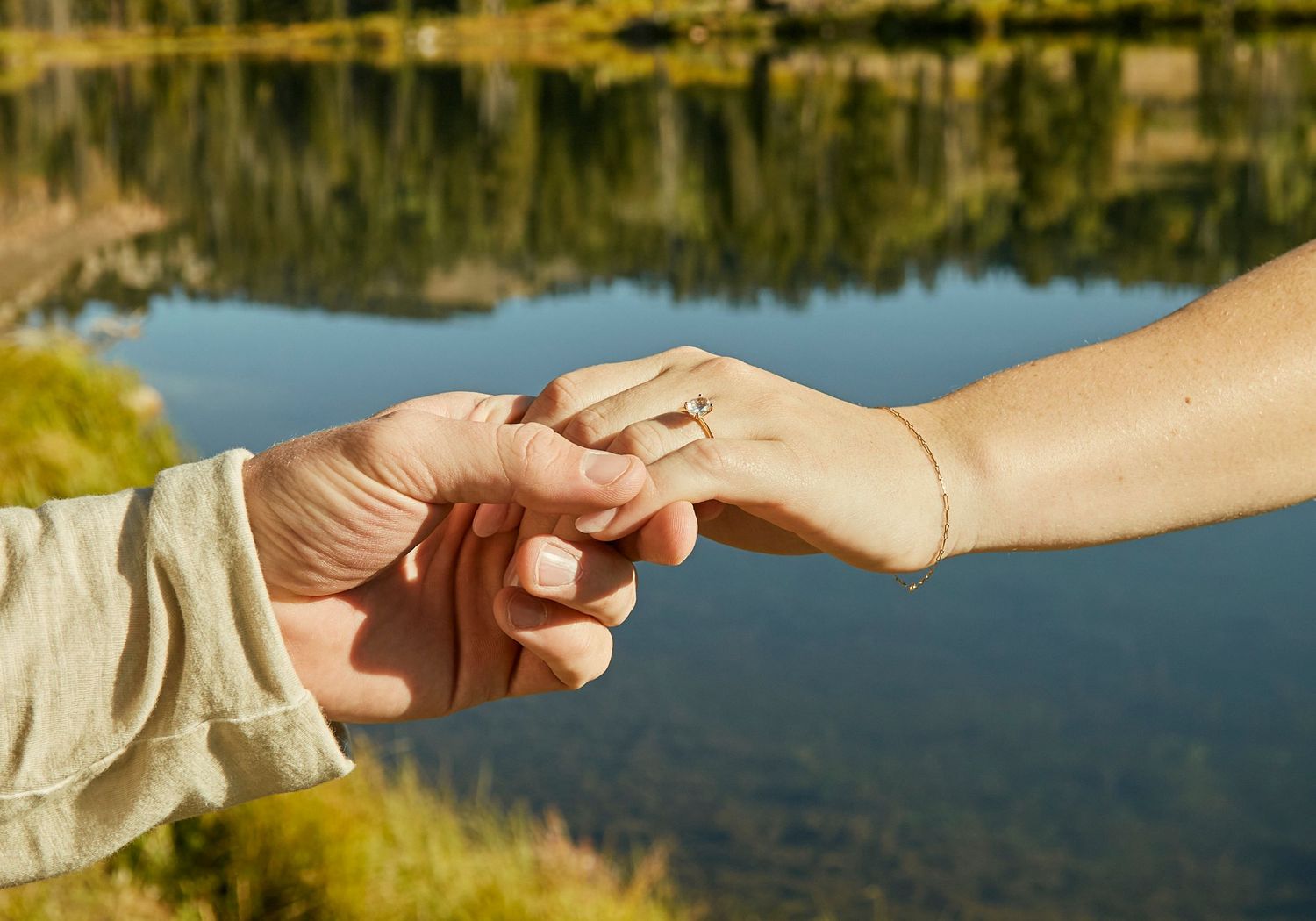 Two hands tenderly clasped together against a sunlit lake backdrop.