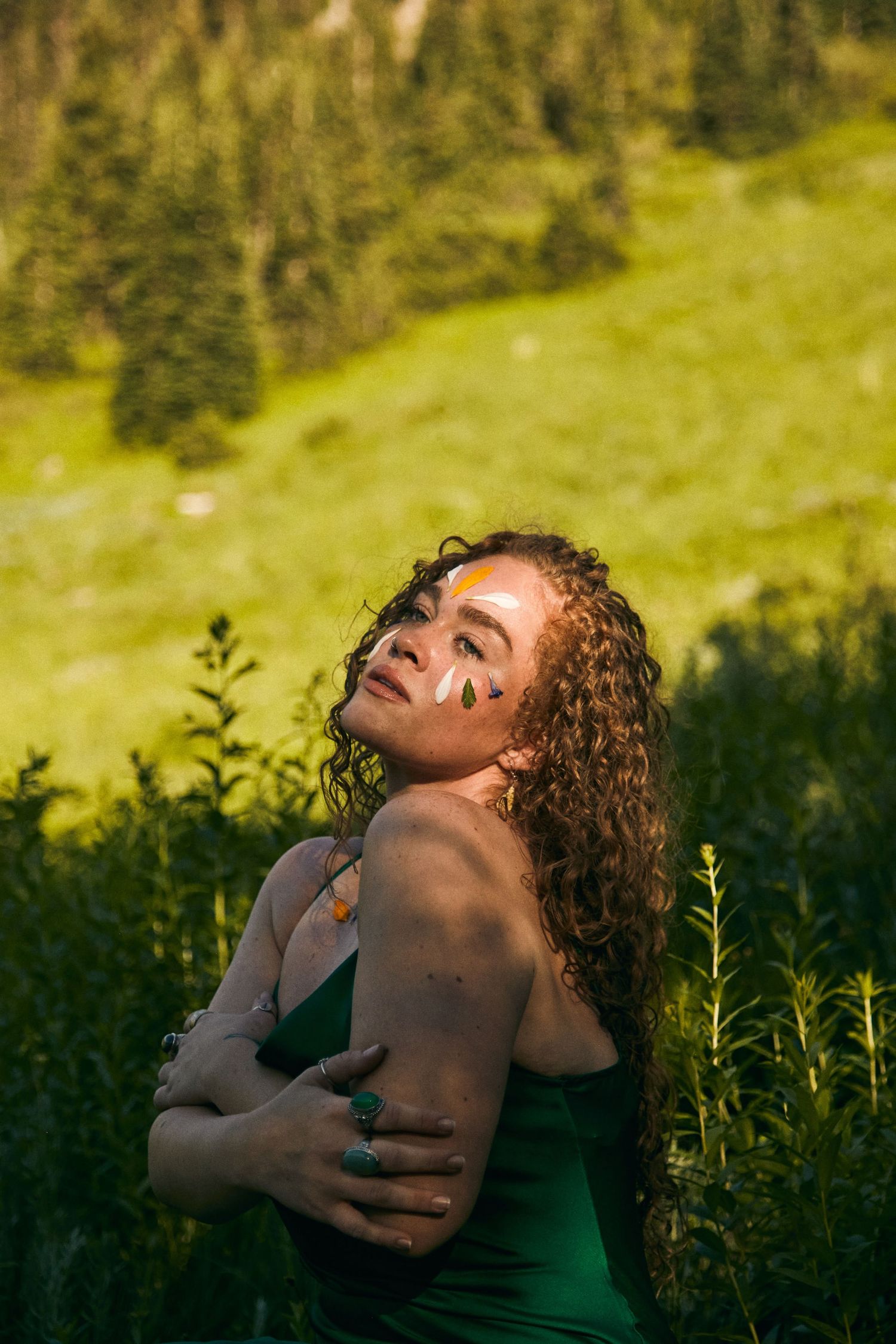 Artistic outdoor portrait with face paint in a sunlit mountain meadow.