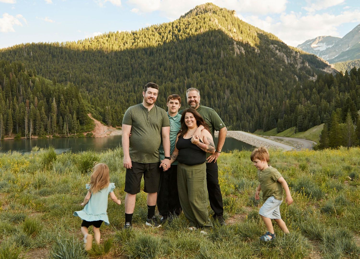 Family photo in mountain meadow with lake and peaks in background during golden hour.