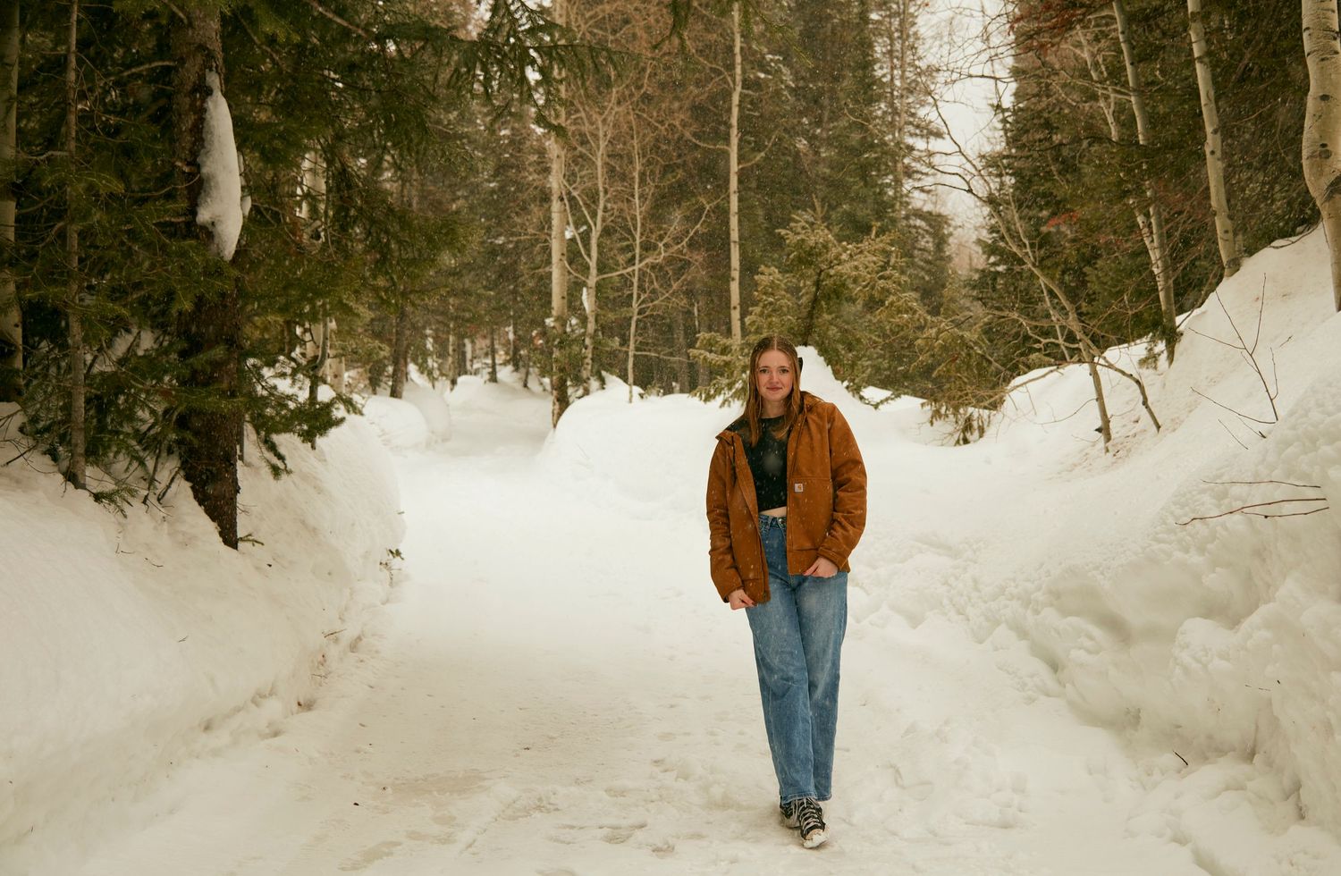 Person in brown jacket walking along snow-covered winter path through forest.
