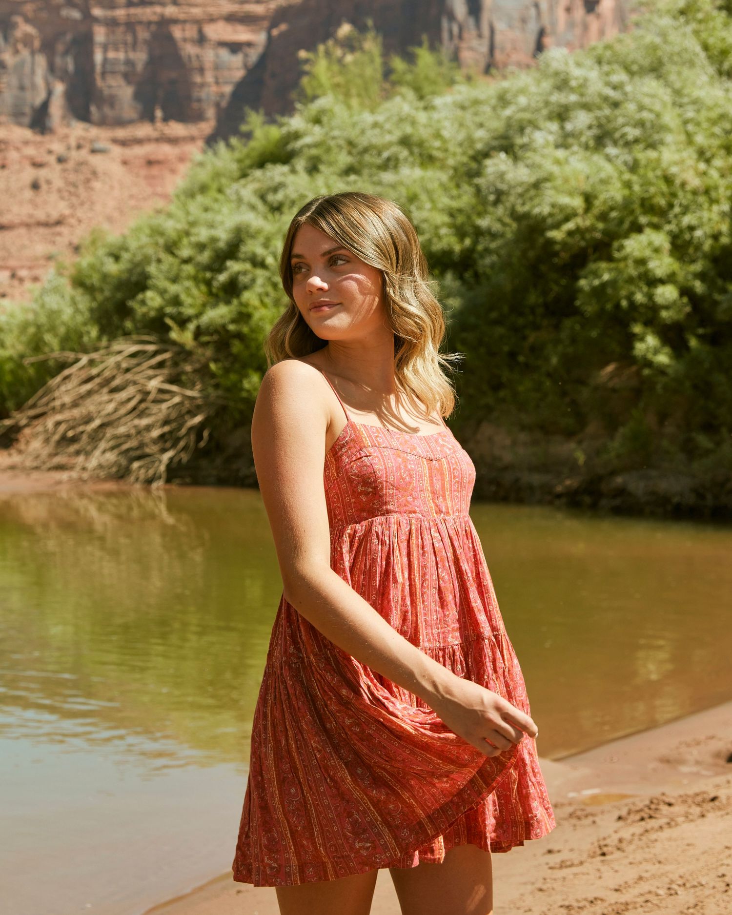Desert canyon landscape portrait featuring coral sundress by river's edge.