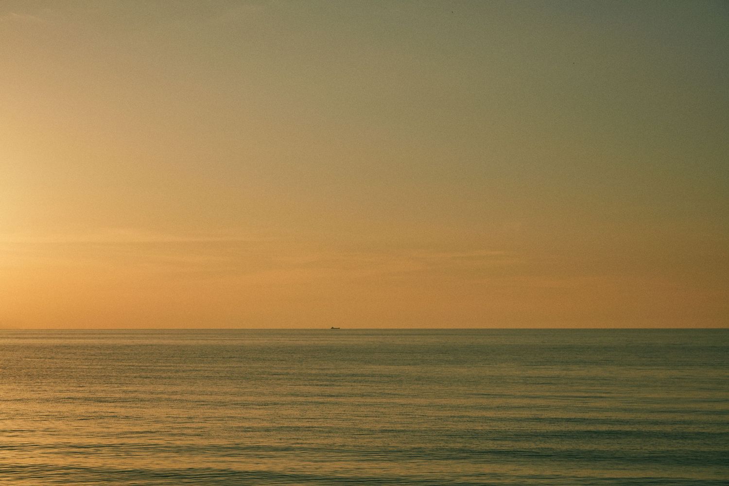 Minimalist seascape at sunset with orange sky melting into tranquil ocean waters.