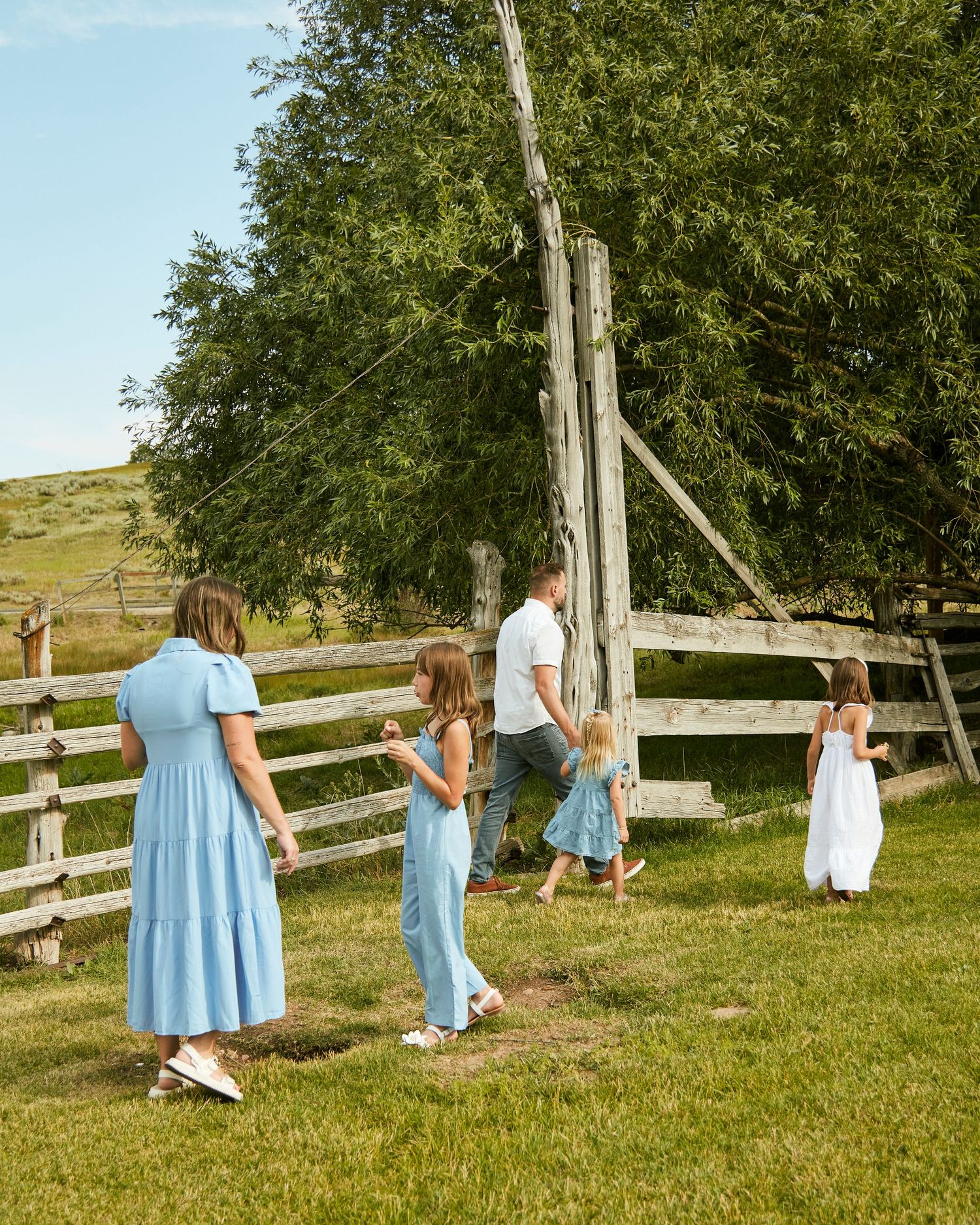 People in coordinated blue dresses walking along rustic wooden fence in countryside.