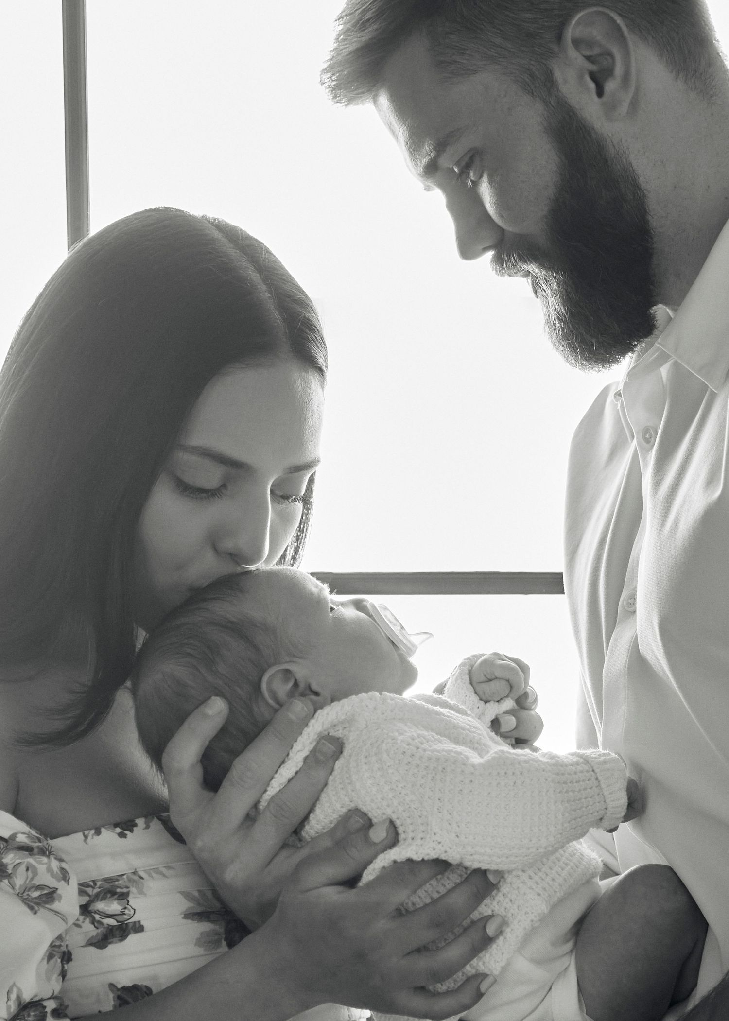 Loving parents share tender moment with newborn baby in black and white portrait.