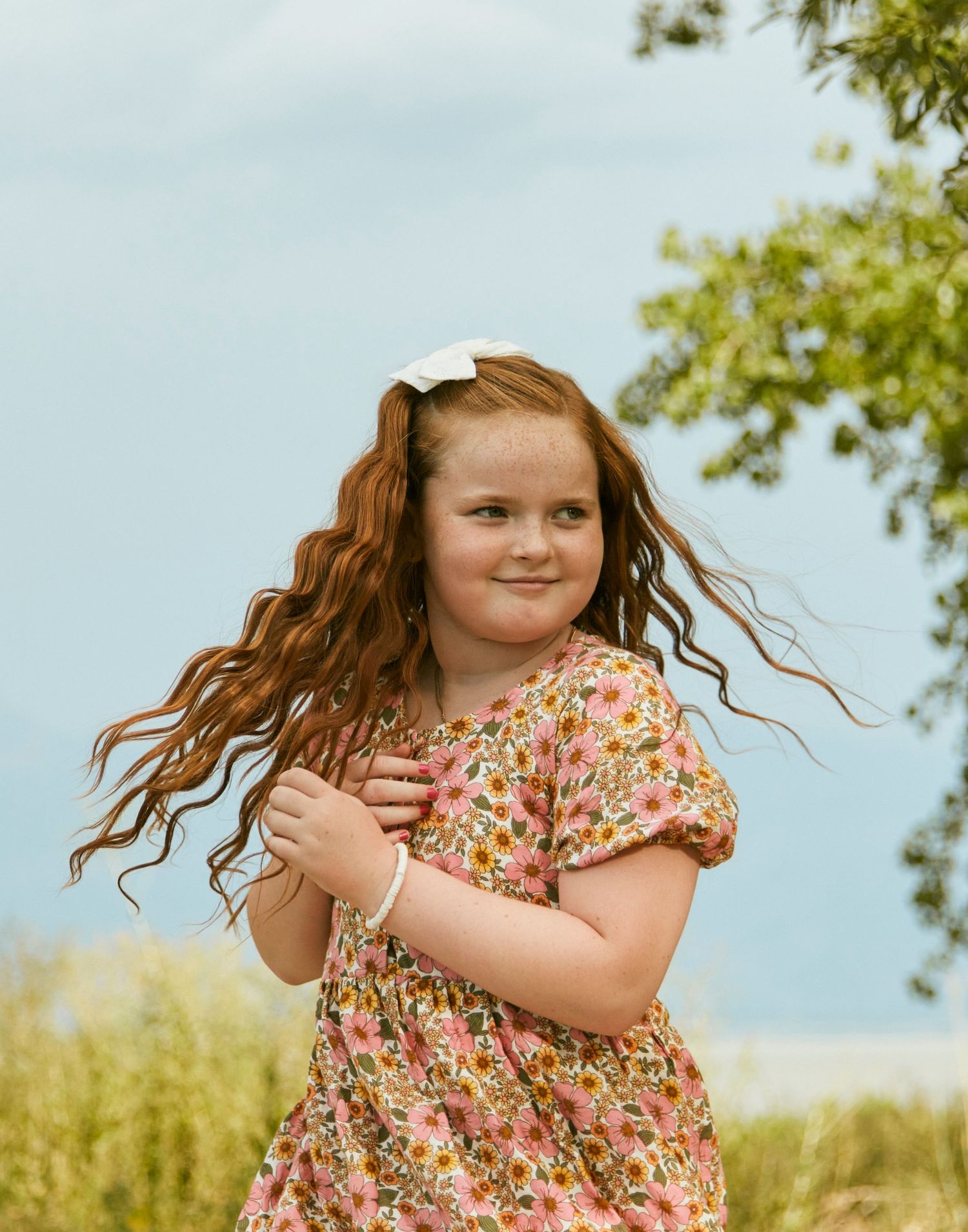 A summer portrait in a floral dress with flowing hair against a blue sky.
