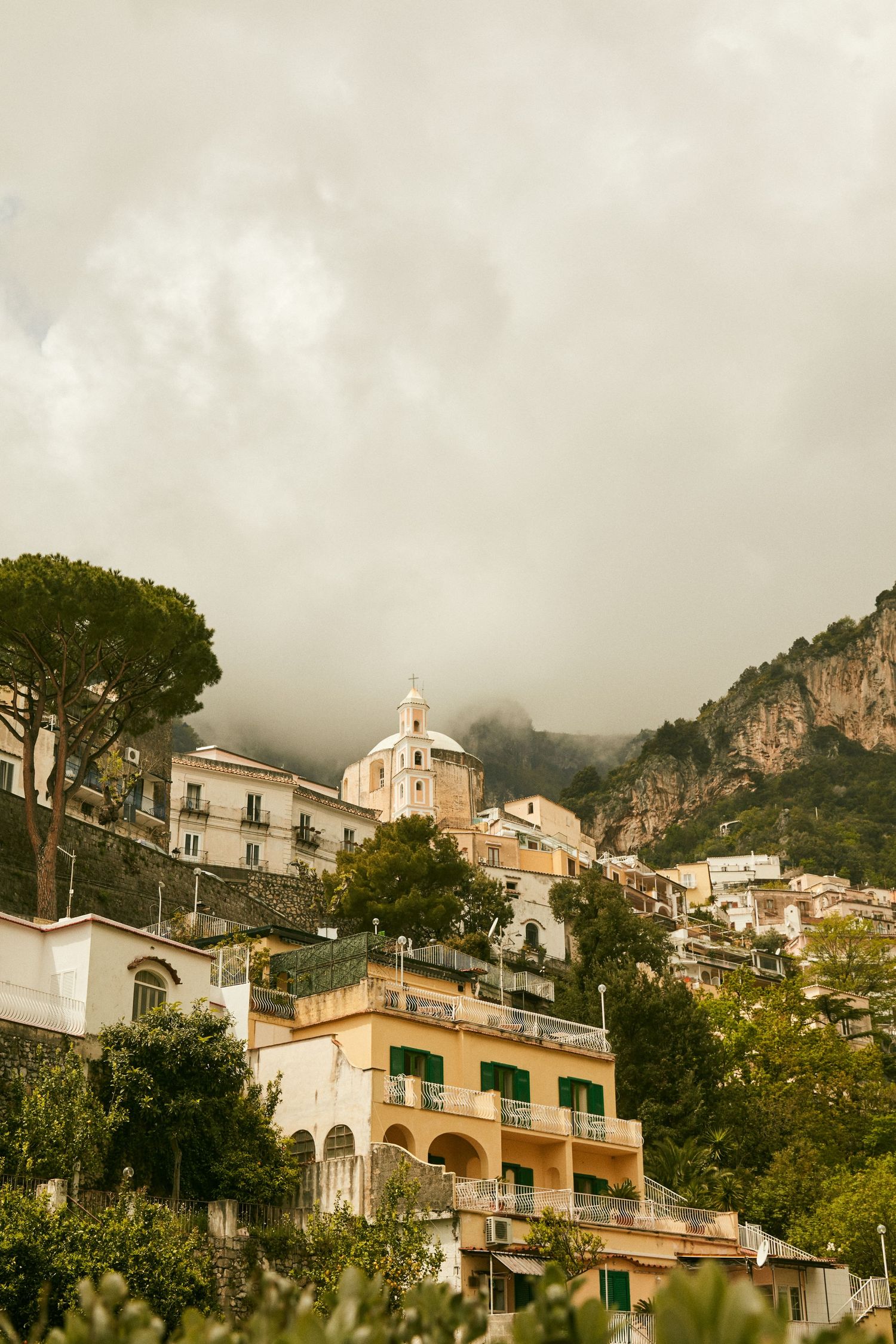 Picturesque hillside town in Amalfi Coast with church and colorful buildings against cloudy sky.