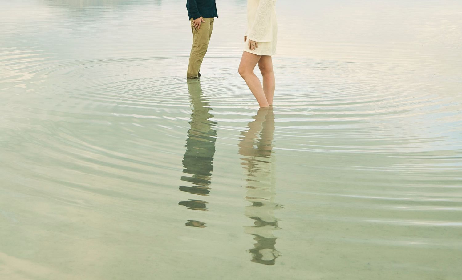 Close-up of two pairs of legs standing in reflective water.