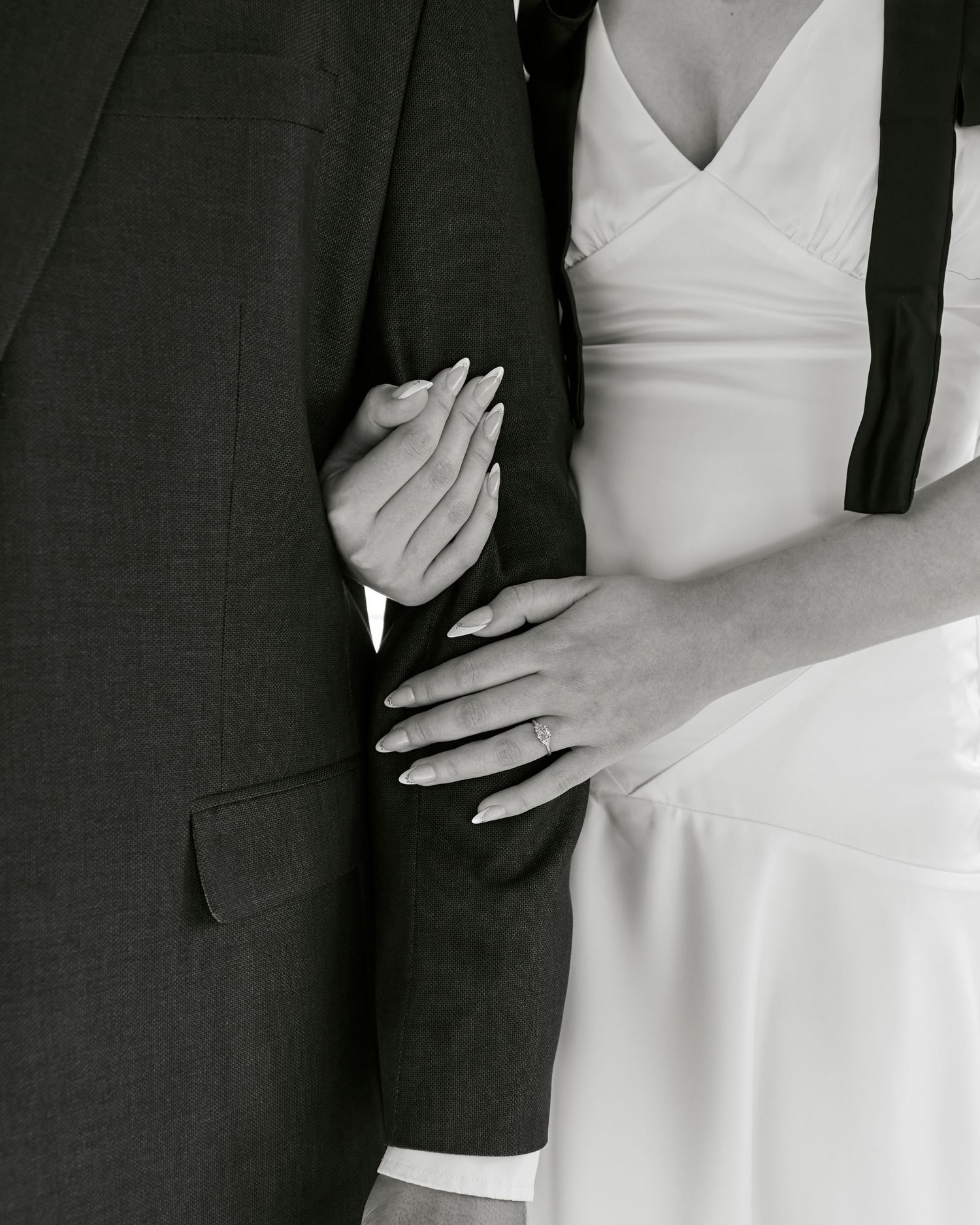 Close-up black and white photo of a couple embracing, showing details of a white wedding dress and dark suit.