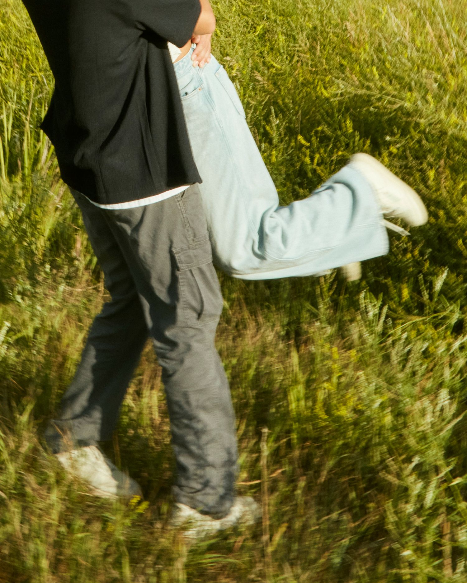 Couple's legs visible in tall grass during playful moment outdoors.