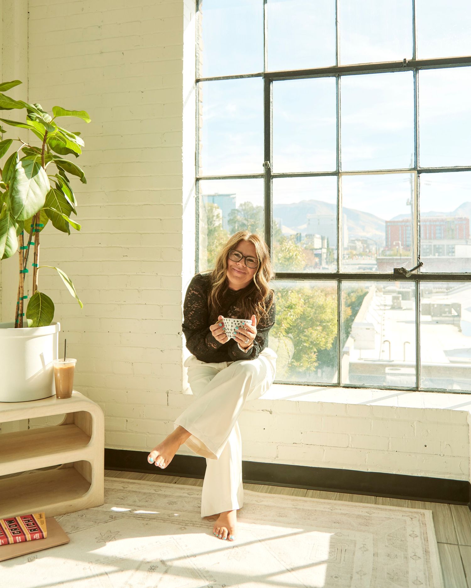 Sunlit corner with large windows, houseplants, and casual seating area.