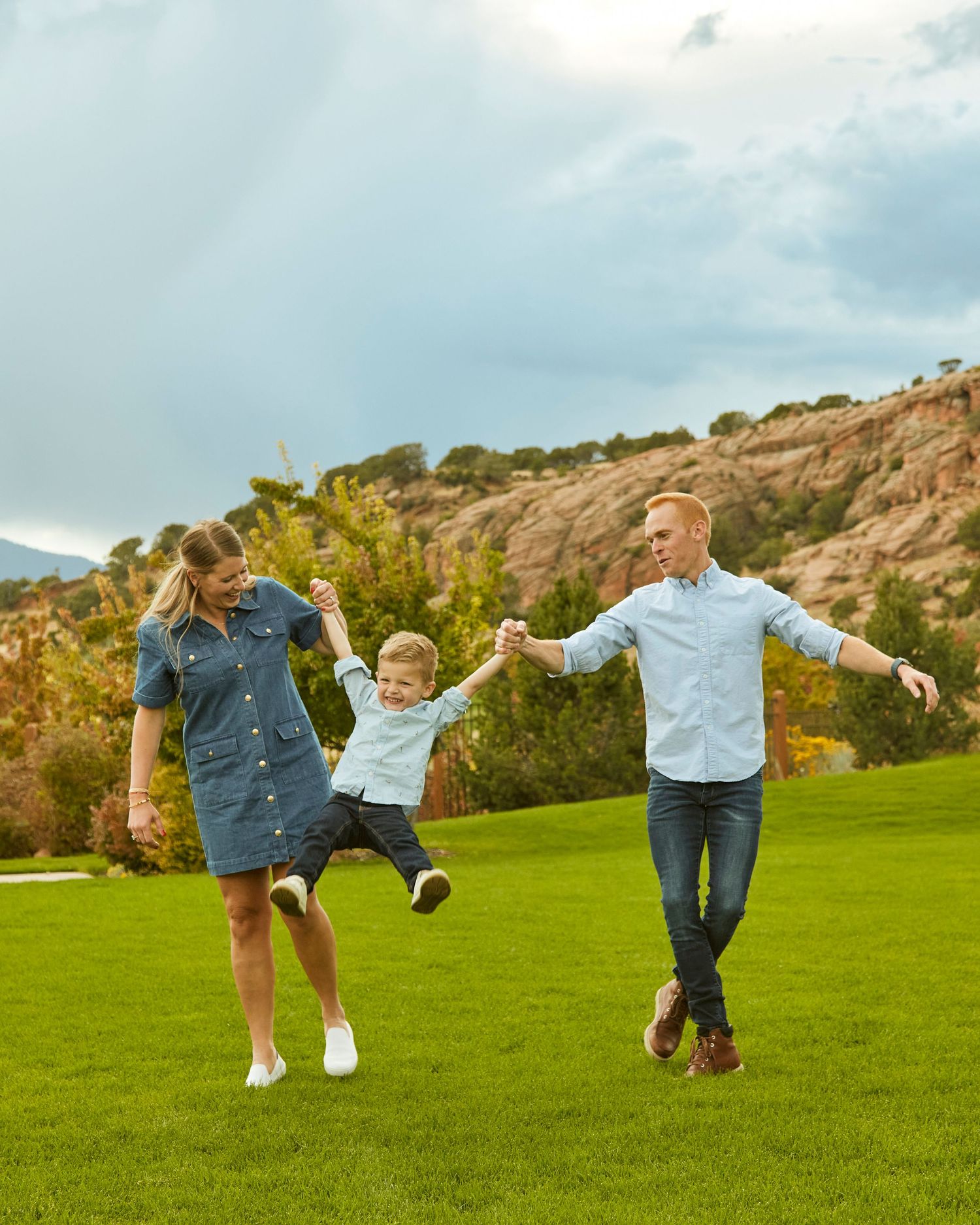 Family jumping and playing together on green grass with mountains in background.