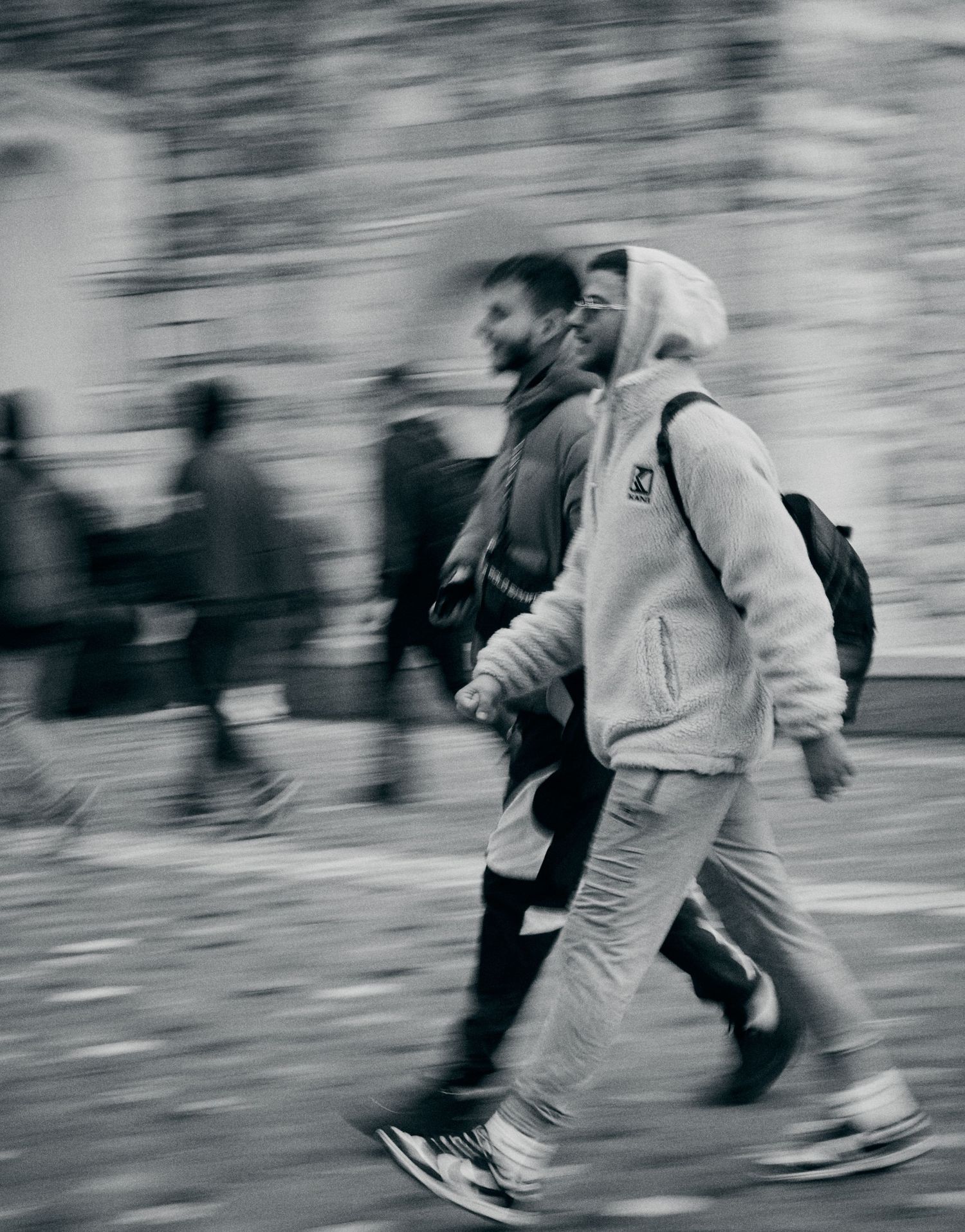 Motion-blurred street photography in black and white showing pedestrians walking.