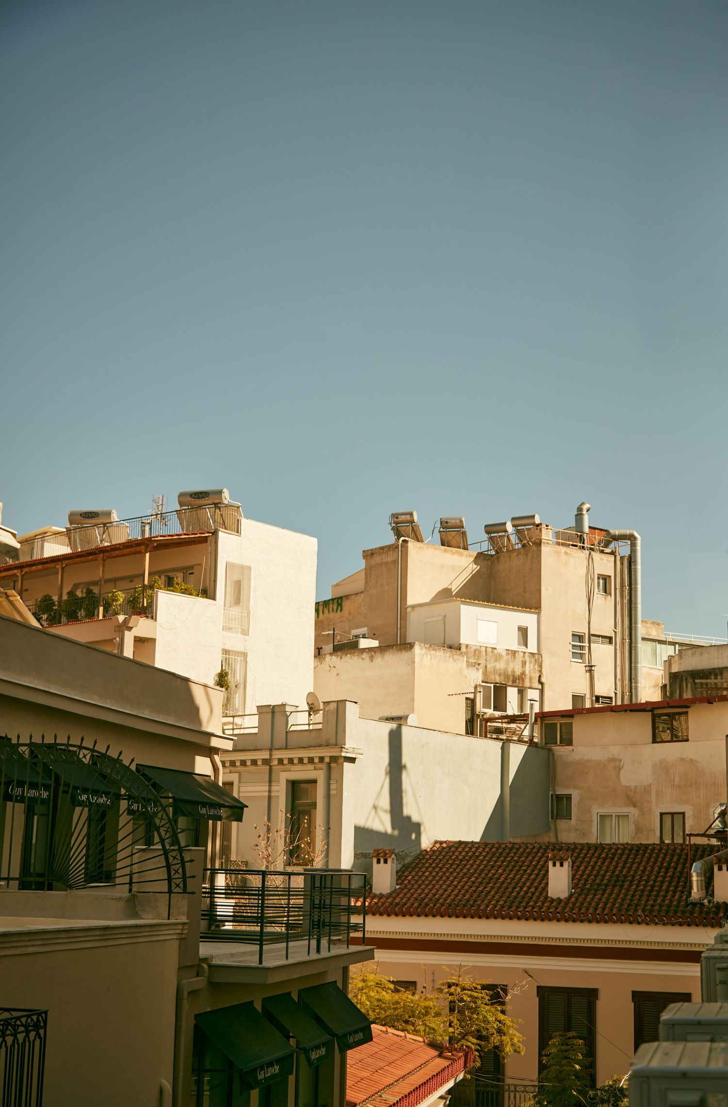 Mediterranean architectural cityscape with tan buildings and rooftops against a blue sky.