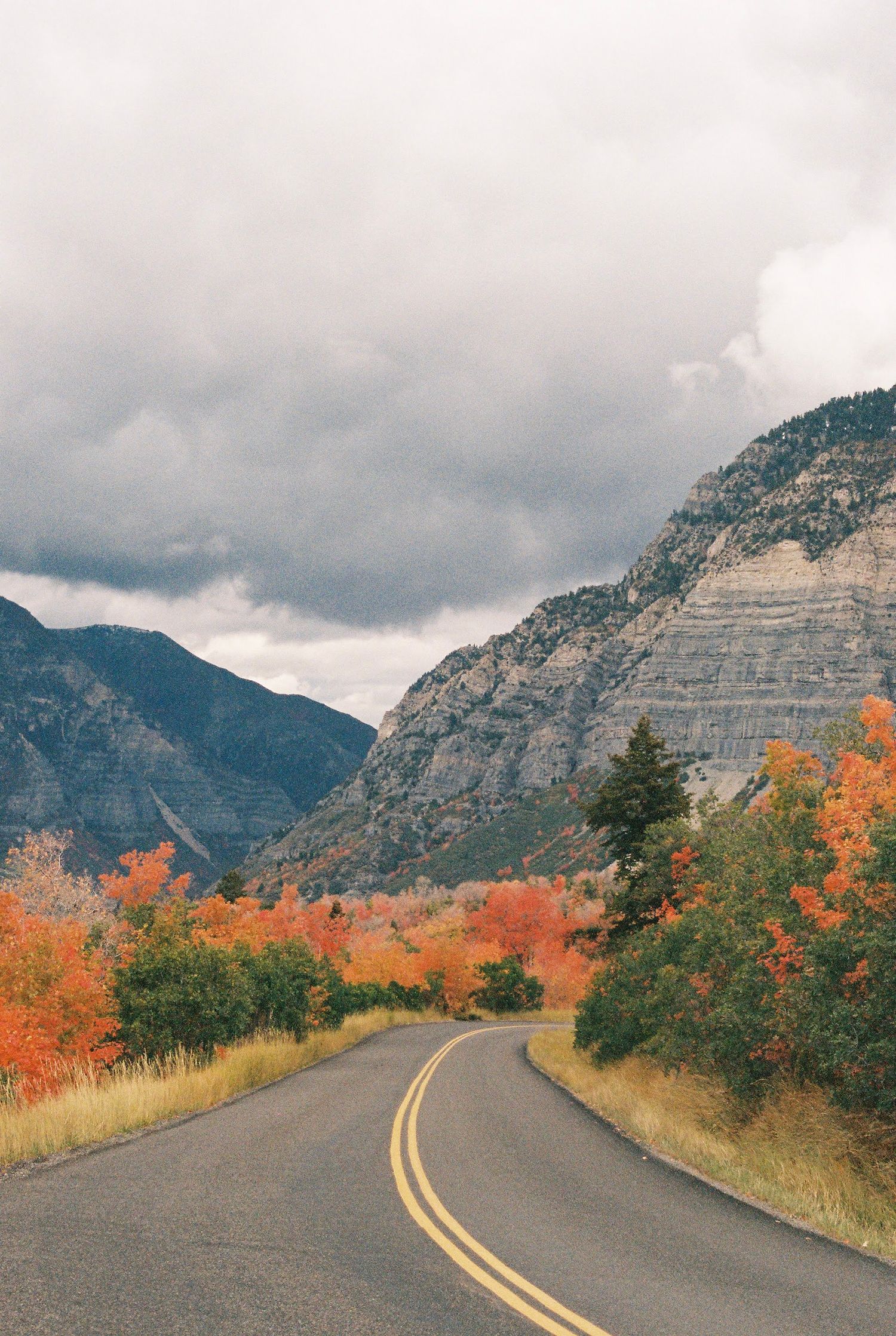 Winding mountain road with vibrant fall foliage and dramatic cloudy sky.