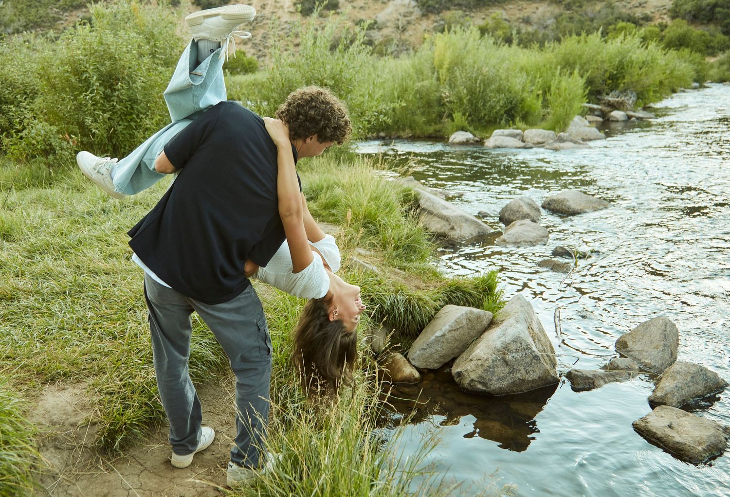 Couple enjoying a playful moment by a rocky stream surrounded by greenery.