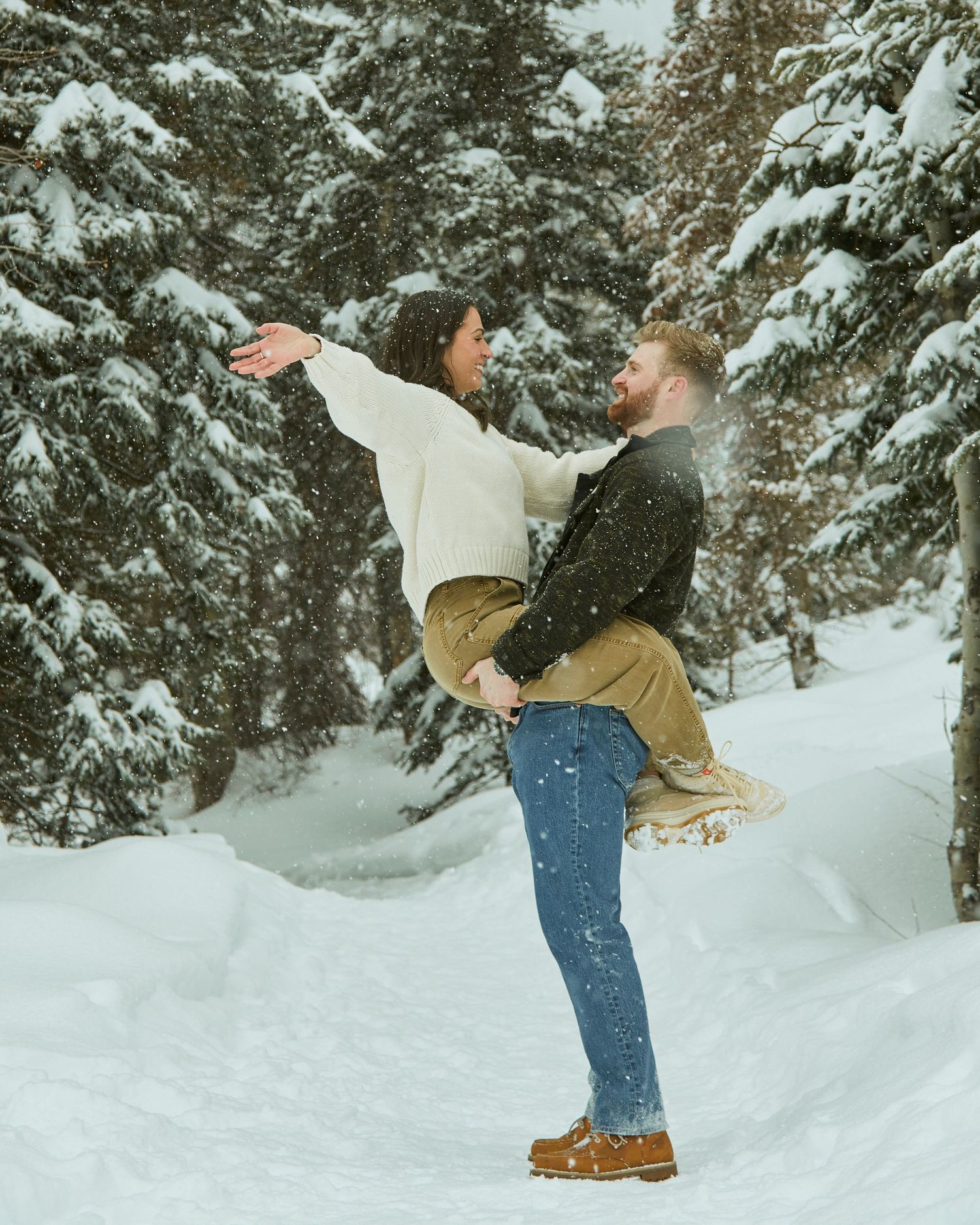 Romantic lift pose in snowy forest setting with evergreen trees.