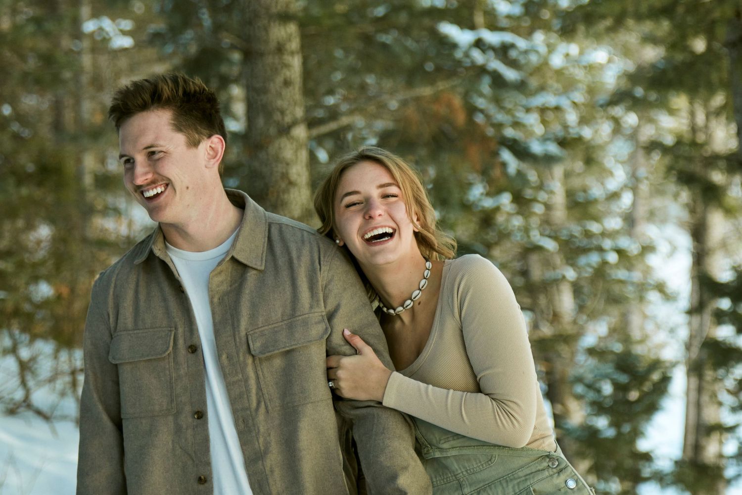 Joyful couple sharing genuine laughter in winter forest engagement session.