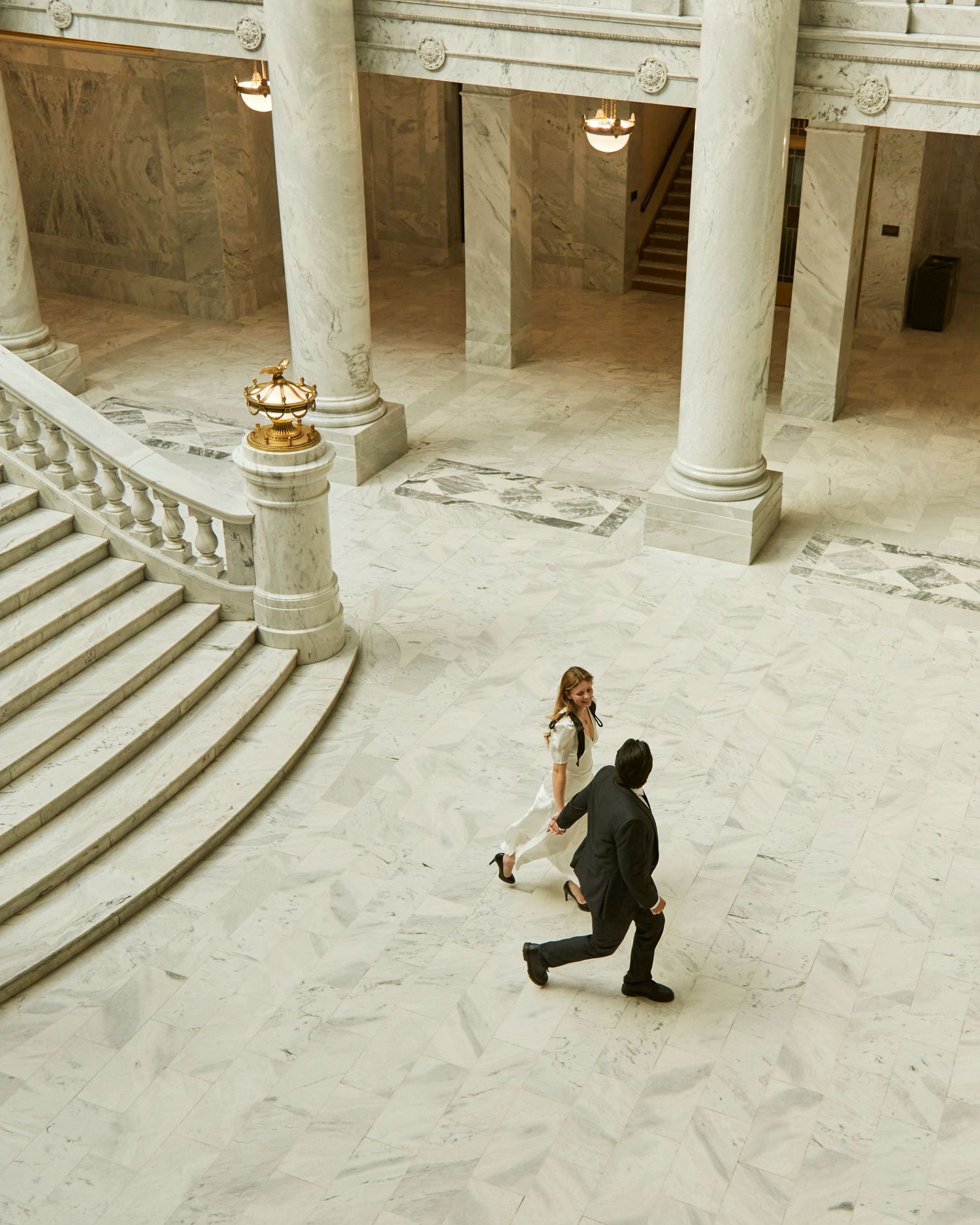 A couple walking in a grand historic building with ornate columns and staircases.