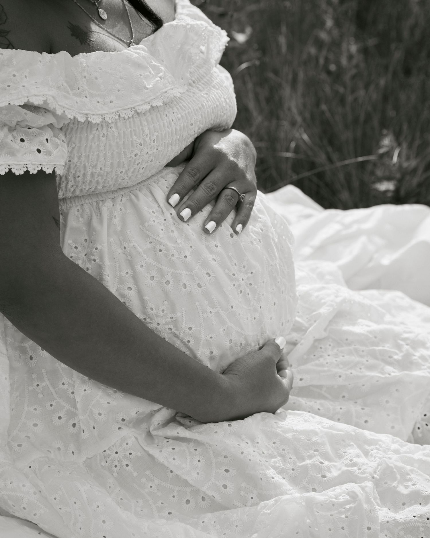 Black and white close-up of hands resting on a maternity dress with delicate eyelet details.