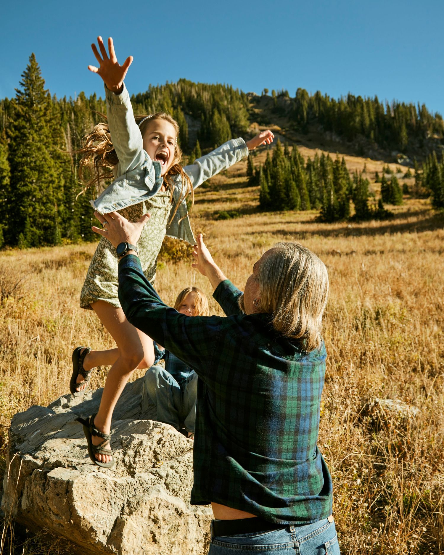 Playful moment captured on mountain rock with evergreen forest backdrop.