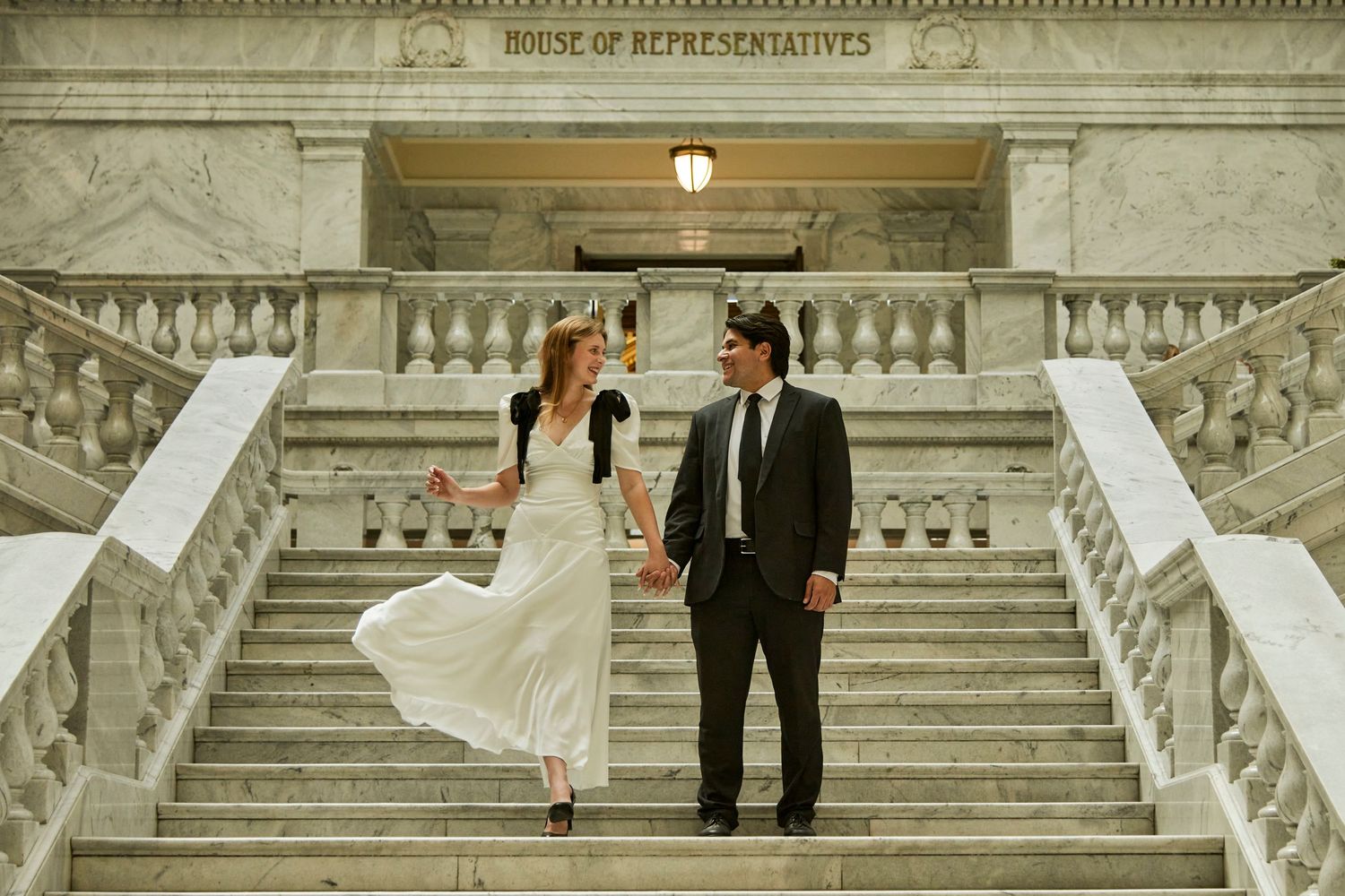 A couple on elegant stone steps of a classical building in wedding attire.
