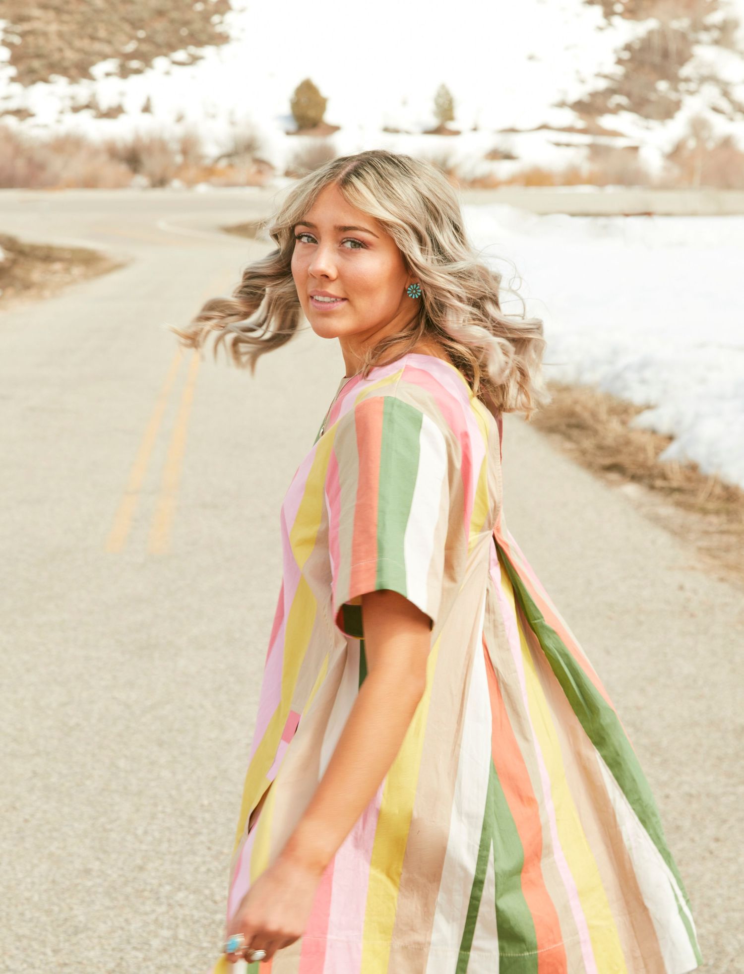 A fashion portrait showing a colorful striped dress against a winding road backdrop.