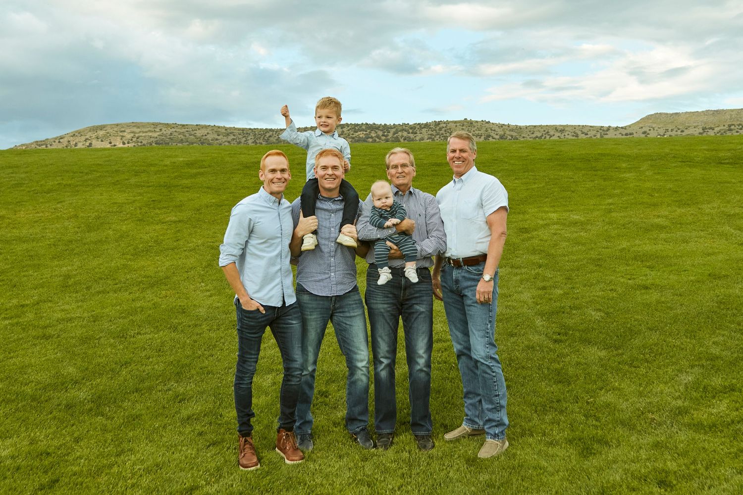 Group standing together on green hillside under cloudy sky in outdoor setting.