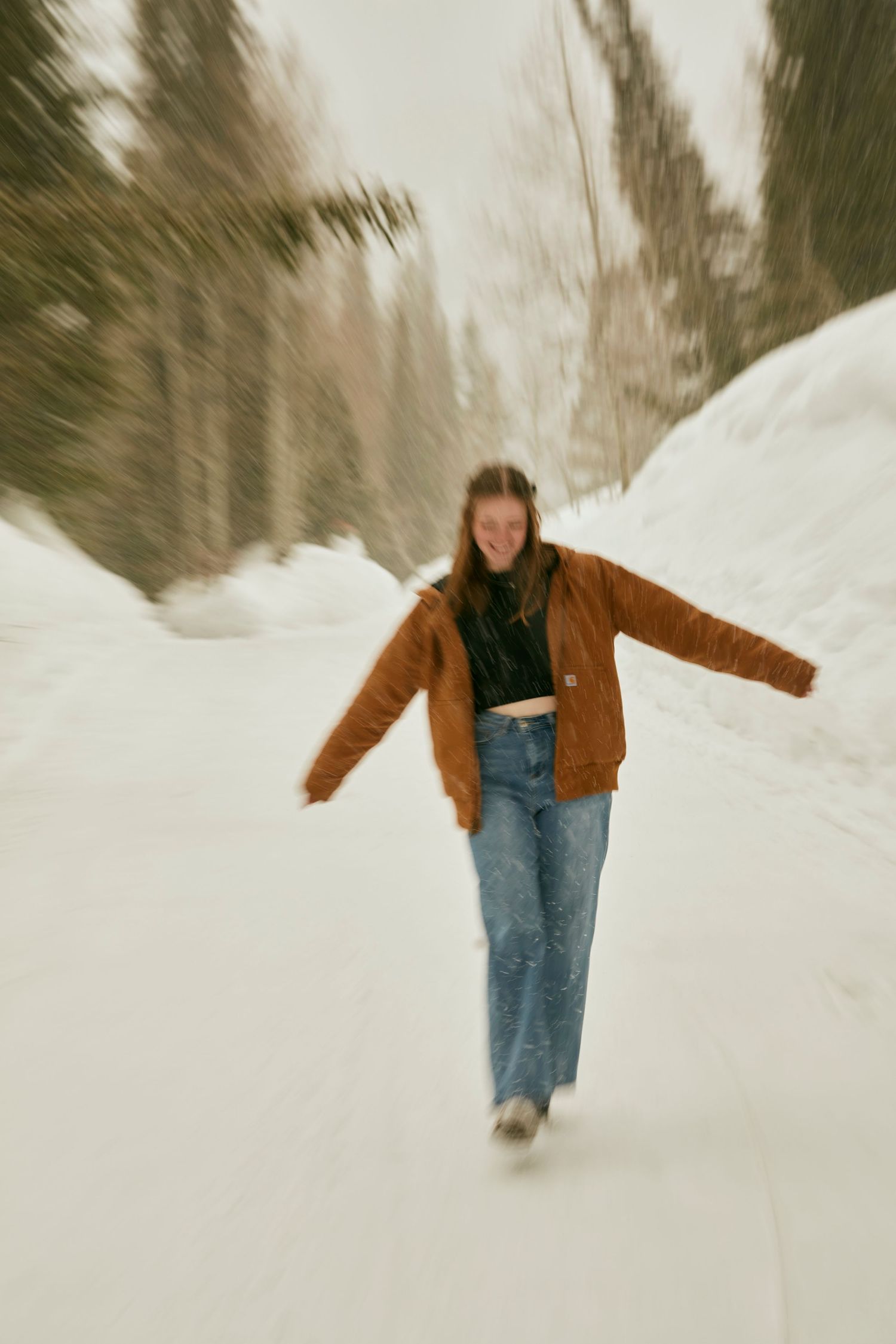 Person walking on a snowy path wearing brown jacket and jeans with motion blur effect.