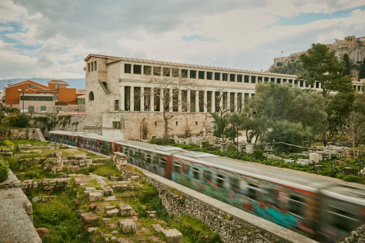 Modern train passing ancient ruins and gardens in Athens, Greece.