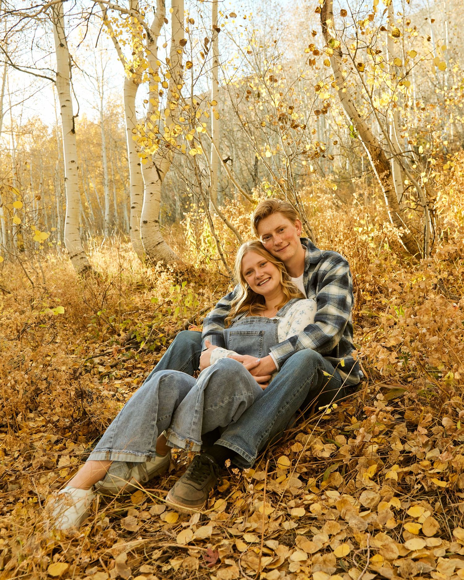 Couple relaxing together on autumn leaves surrounded by golden aspen trees.