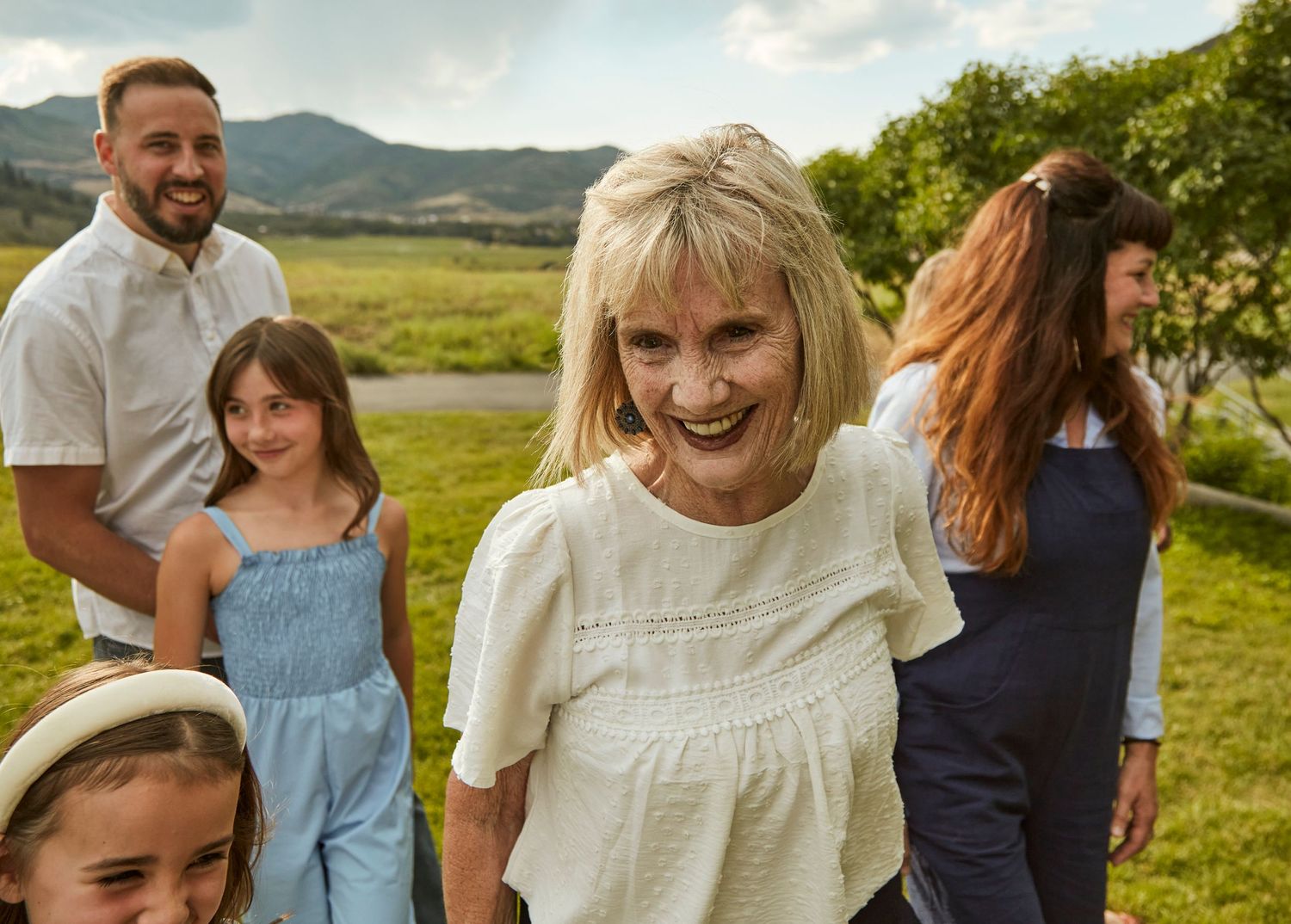 A joyful group poses together in a scenic mountain meadow on a sunny day.