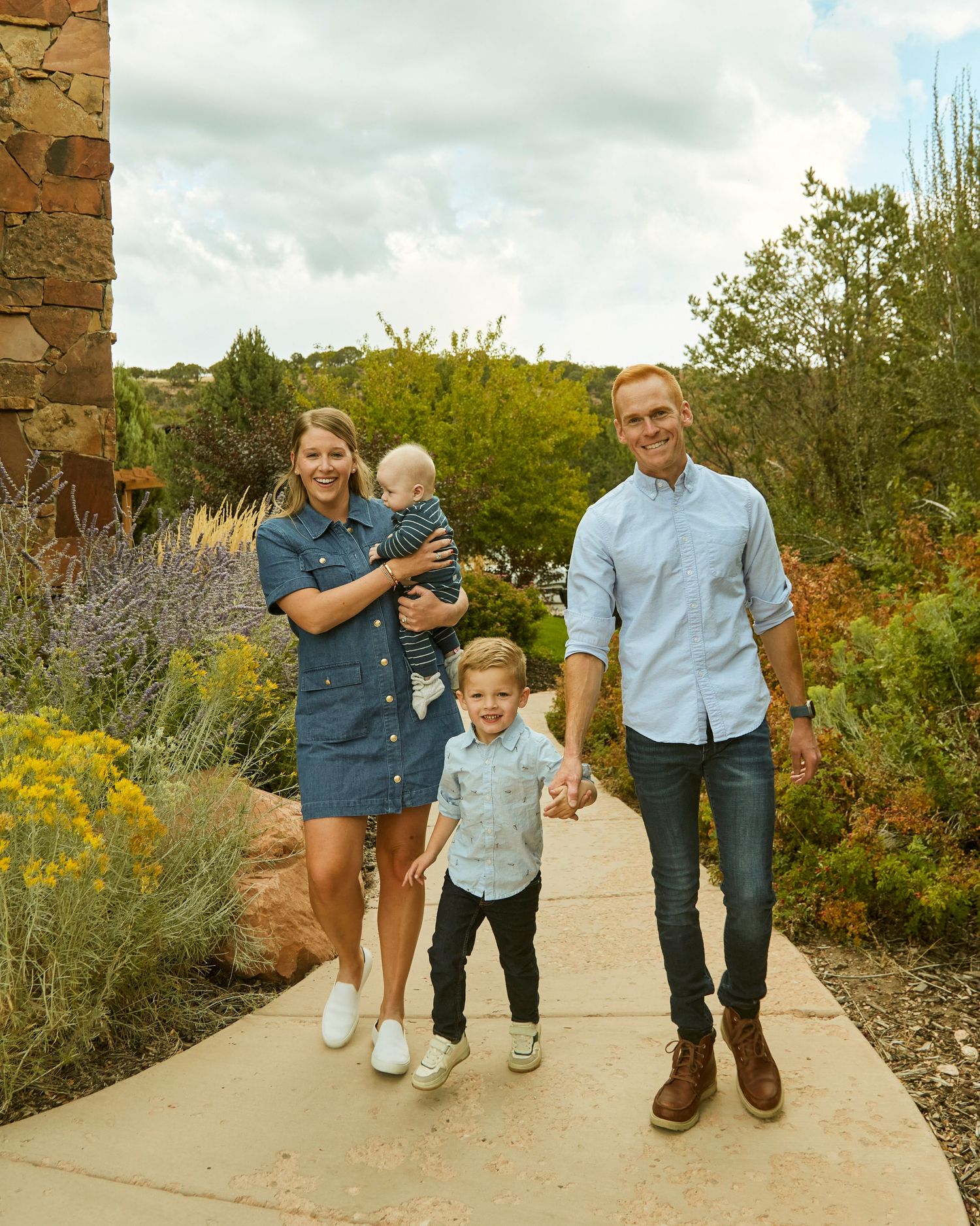 Family walking together on a garden path surrounded by yellow wildflowers and greenery.