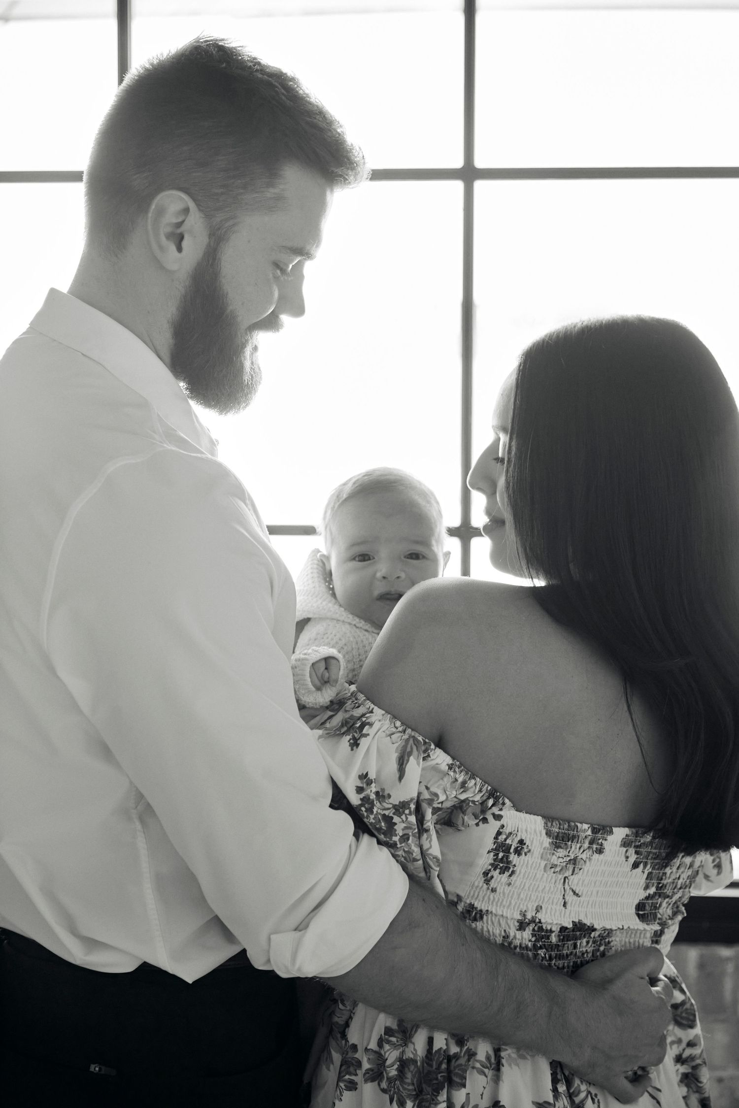 Intimate black and white family portrait by window with natural light.