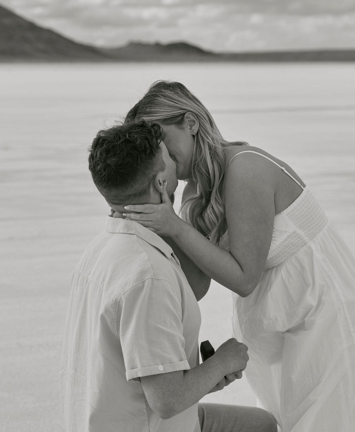 A black and white capture of an intimate moment between newly engaged couple on salt flats.