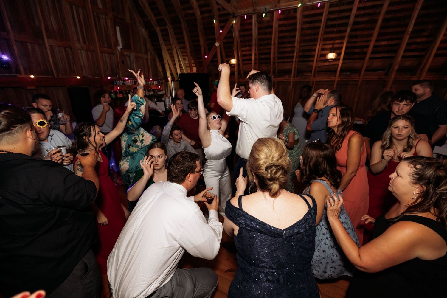 Wedding reception dance party with guests celebrating under barn rafters.