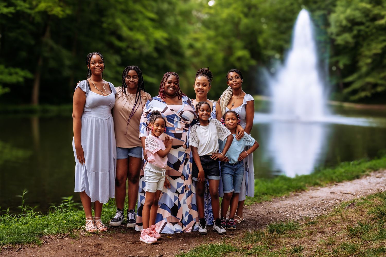 Multi-generational family group poses together by fountain in park setting.