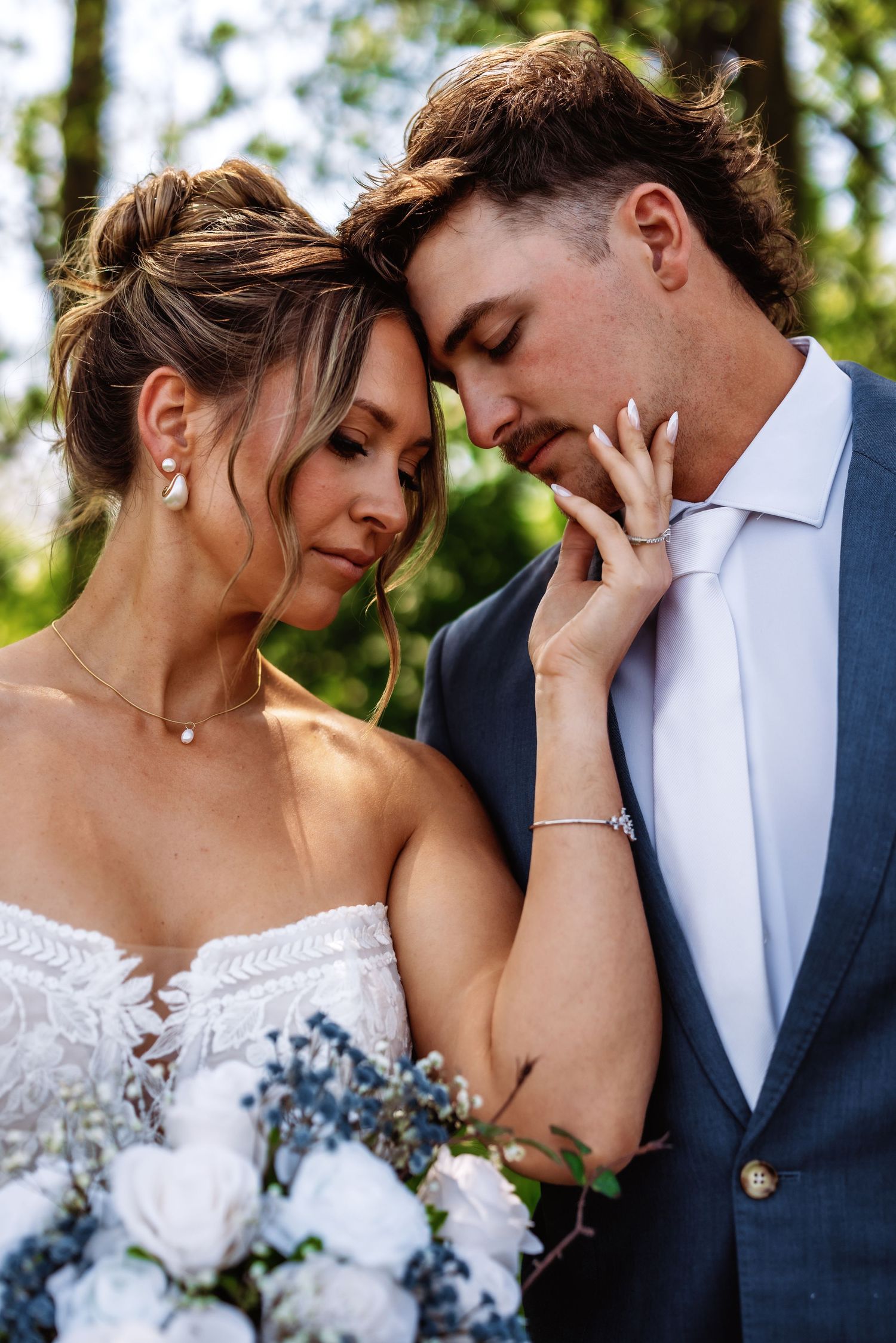 Intimate wedding portrait of a couple embracing outdoors with the bride holding white and blue flowers.