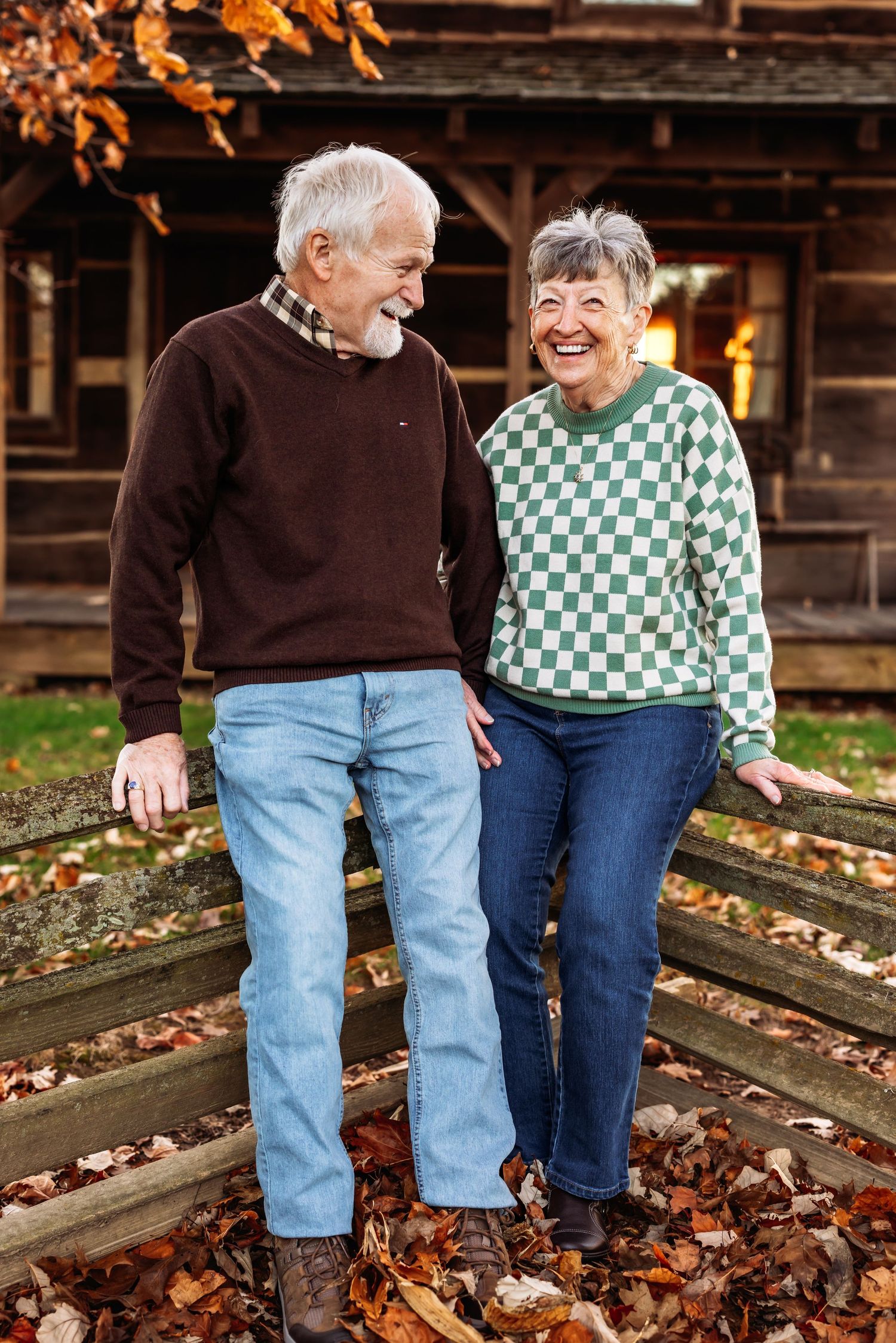 Elderly couple walking through fallen autumn leaves wearing coordinated brown and checkered outfits.