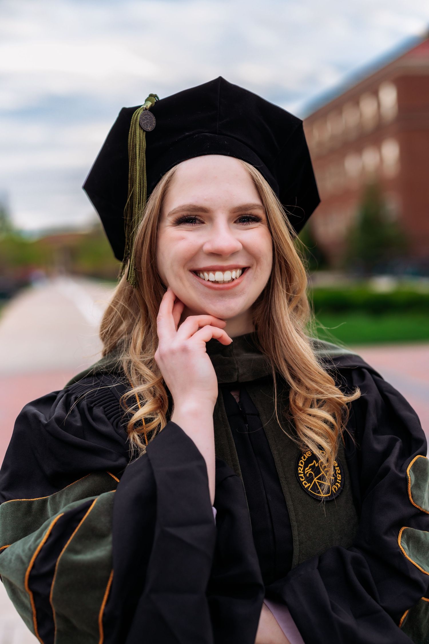 Graduate in black cap and gown with gold tassel smiling during outdoor graduation photos.