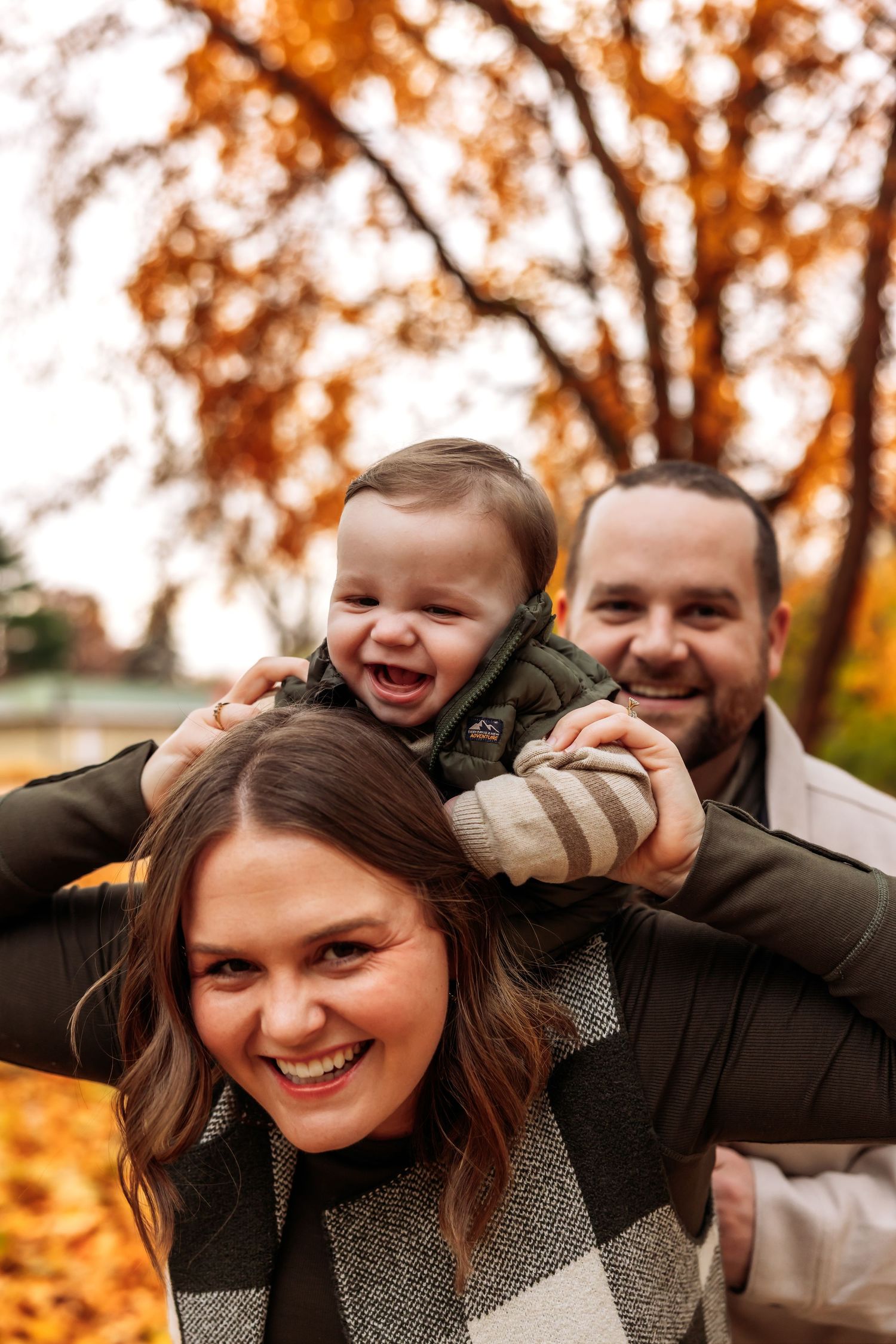 A family enjoys a playful moment together outdoors during autumn with colorful orange foliage in the background.