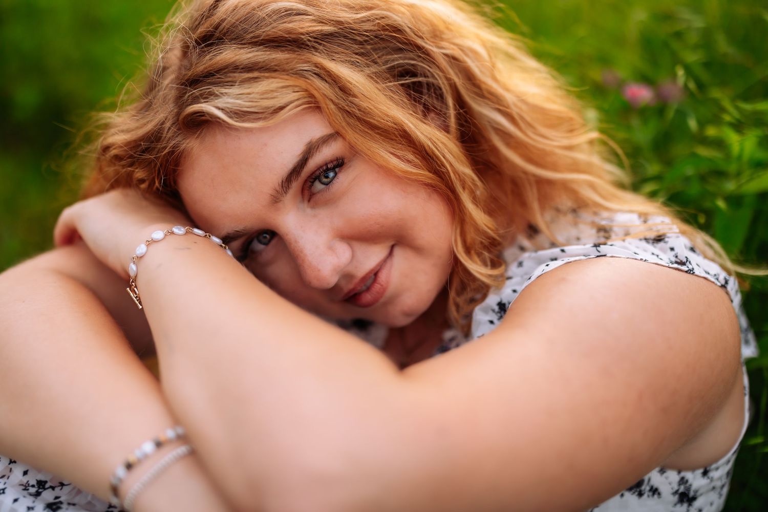 A close-up portrait in a floral dress against a green outdoor background with soft natural lighting.