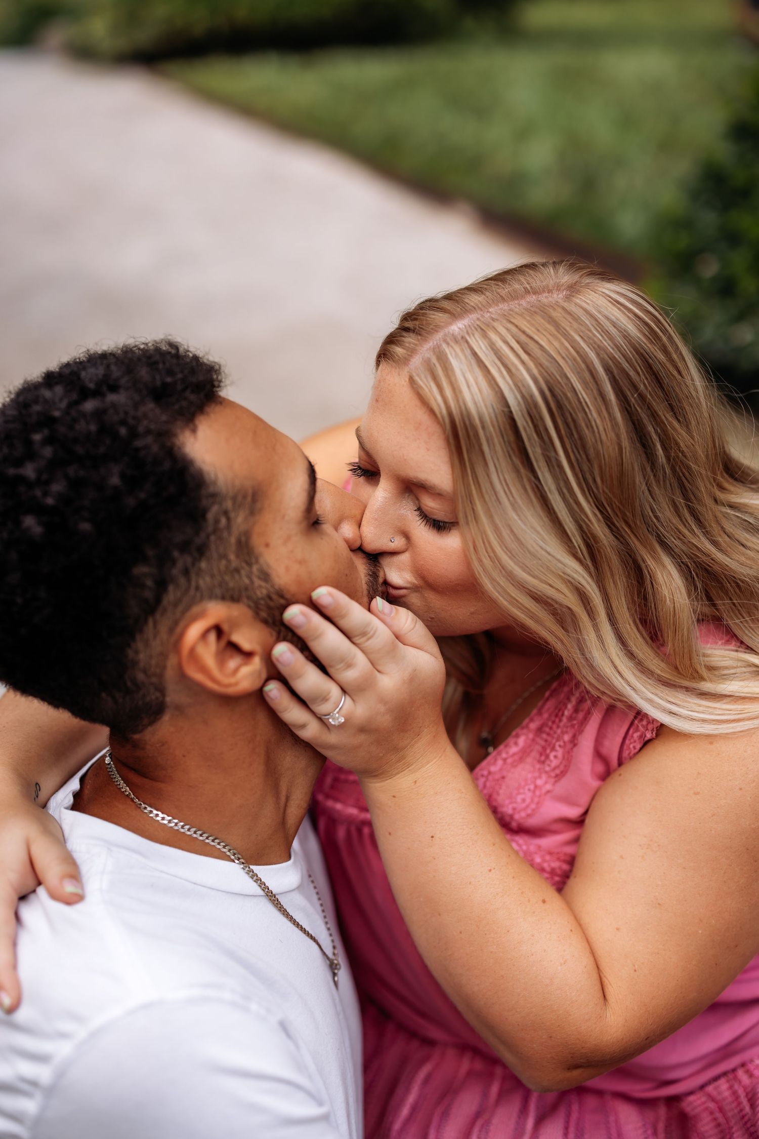 A couple shares a tender kiss on a garden path in summer.
