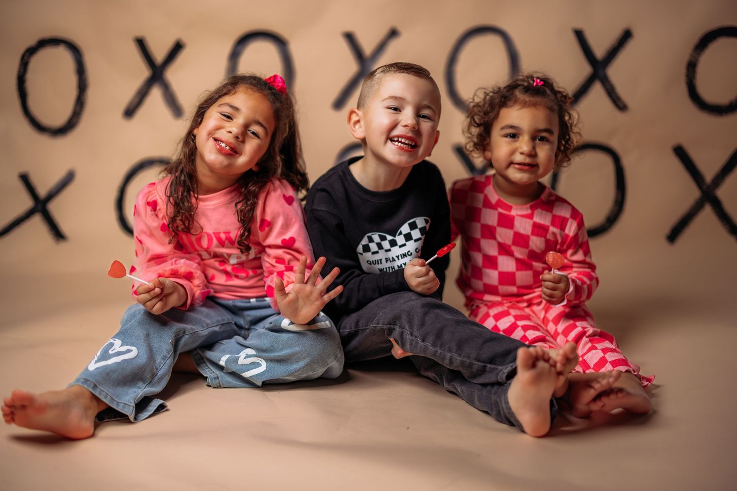 Three children in colorful shirts laughing together against wall with X and O pattern.