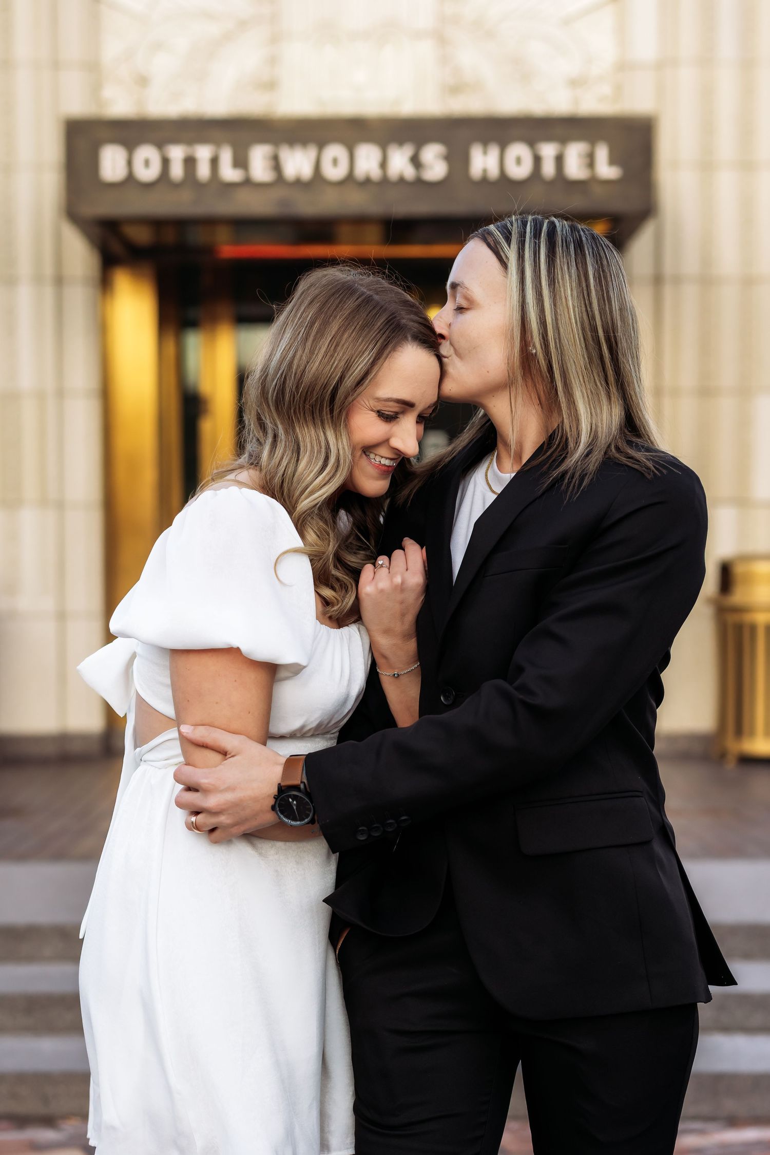 Intimate moment captured outside the Bottleworks Hotel with couple in white dress and black suit.