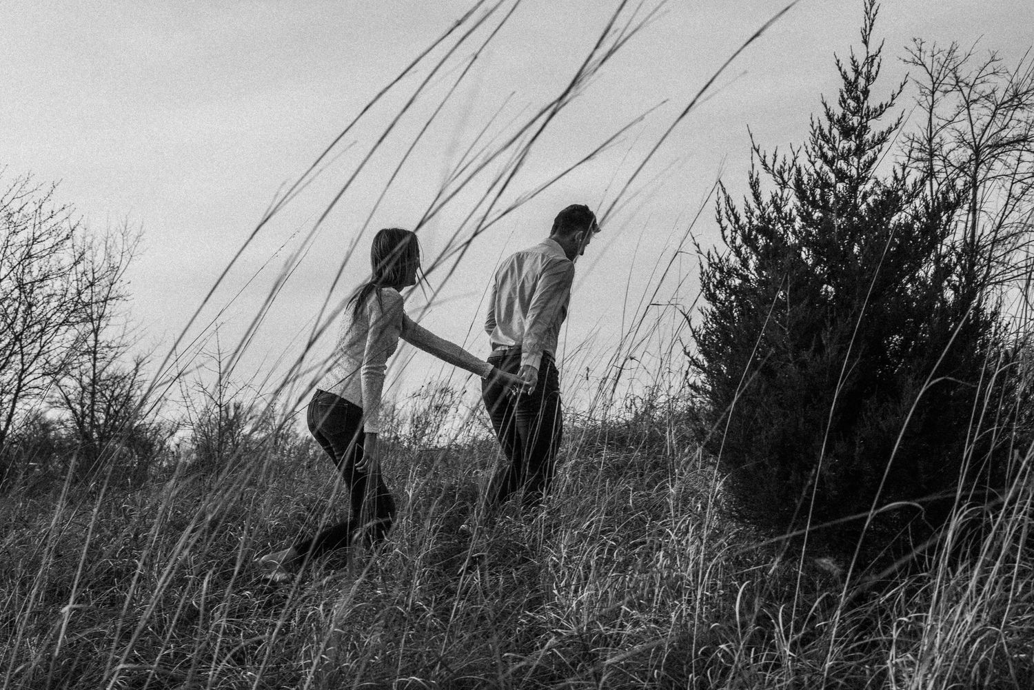 Black and white artistic photo of couple walking through tall grass.